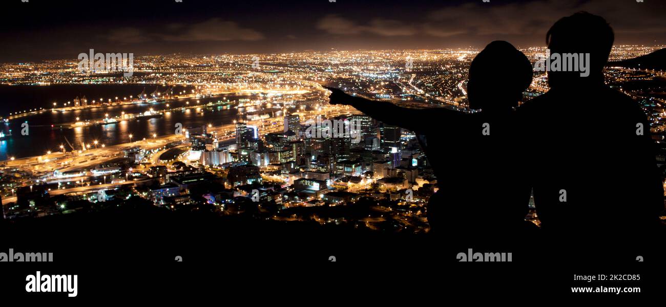 The best seat in the house. Silhouette of a young couple enjoying the city nightscape. Stock Photo