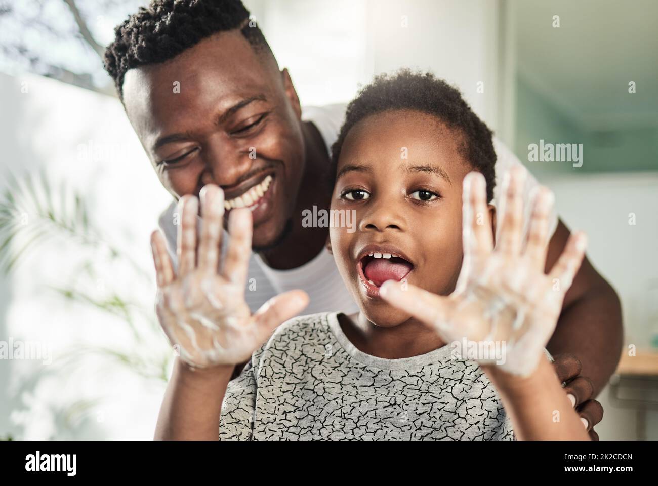 Good hygiene habits will keep you healthy. Portrait of a boy holding up his soapy hands while standing in a bathroom with his father at home. Stock Photo