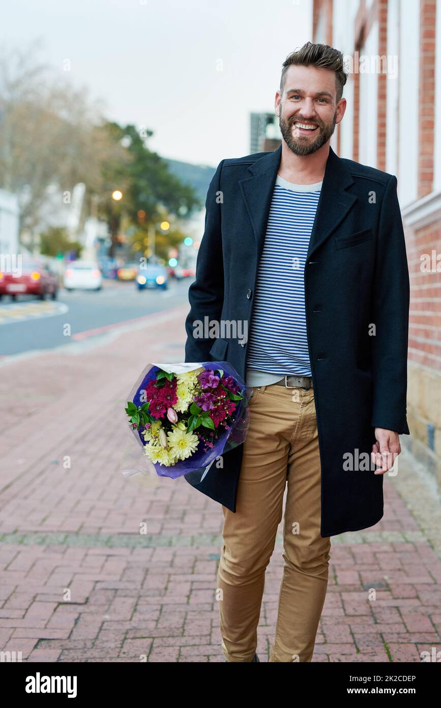 Chivalry isnt dead. Portrait of a handsome young man walking through the city with a bunch of flowers in hand. Stock Photo