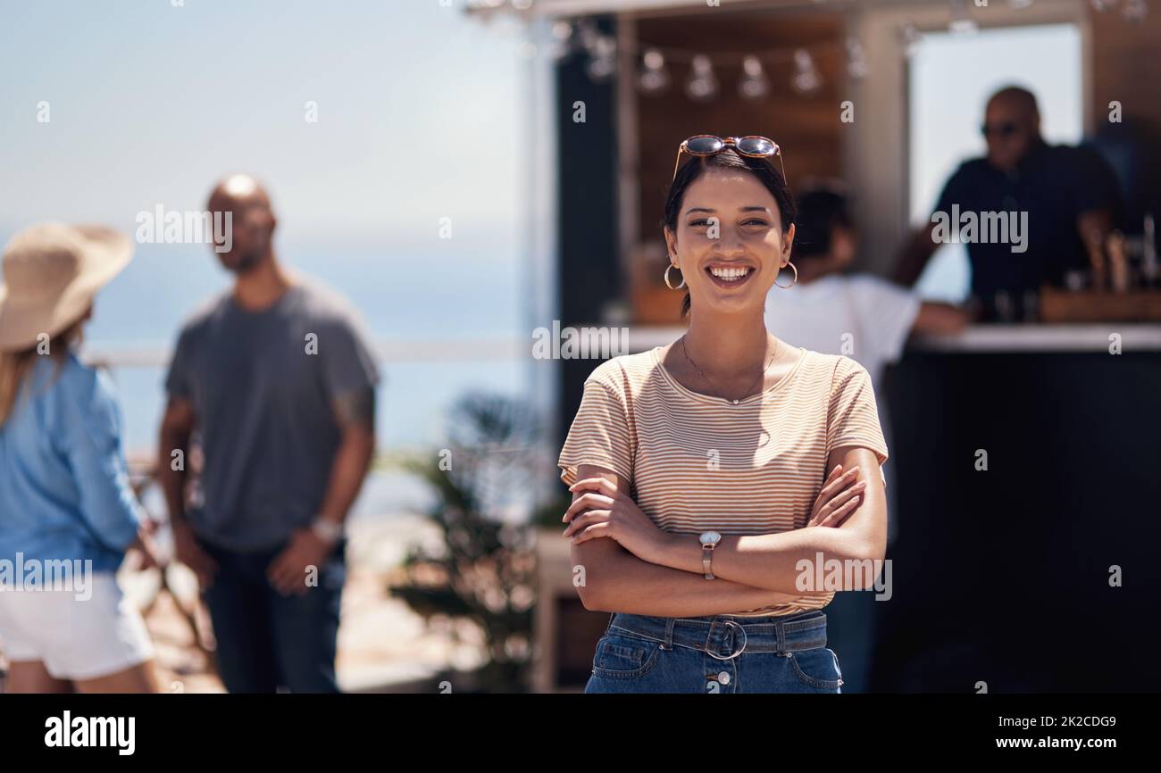 I finally made it. Portrait of a cheerful young woman smiling brightly while standing outside on a beach promenade during the day. Stock Photo