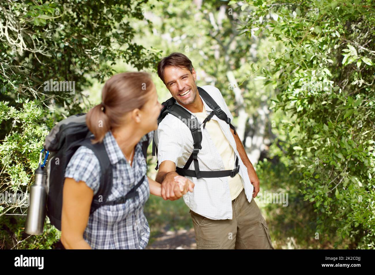 Motivating each other to keep moving. A young man being pulled playfully by his wife with backpacks on their backs. Stock Photo