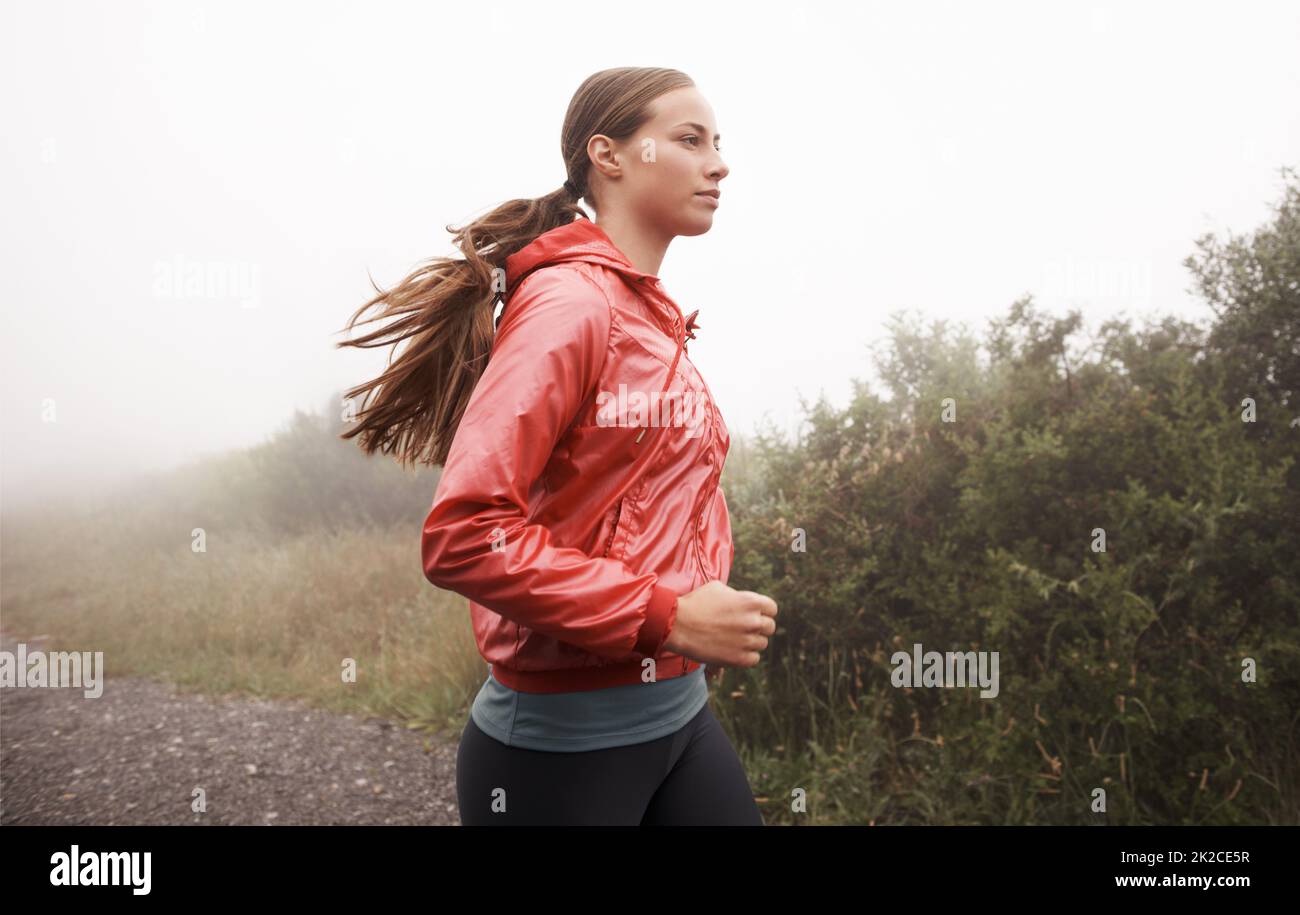The only way to run. Shot of a young female jogger in a misty country road in the morning. Stock Photo