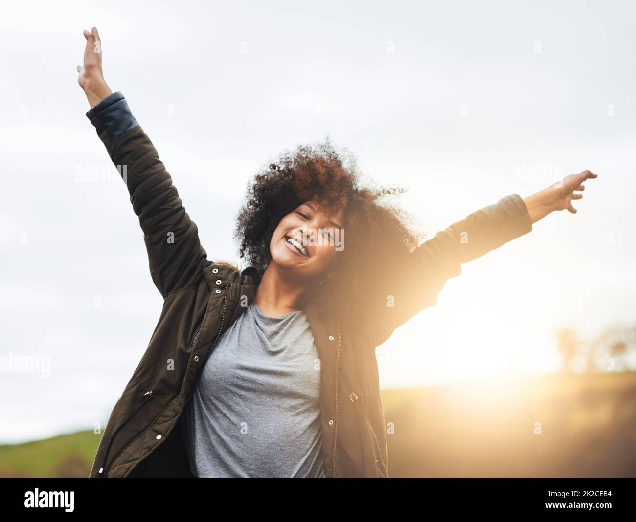 Life is for celebrating. Portrait of a joyful young woman raising her hands in nature. Stock Photo