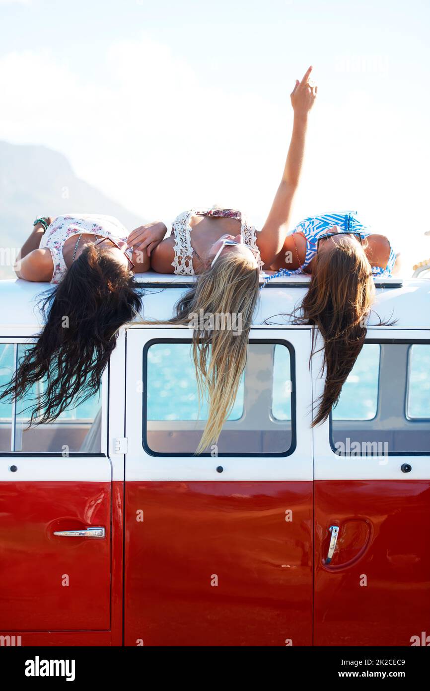 Appreciating the finer things in life. Three young girls rest on top of their van looking at the sky - copyspace. Stock Photo
