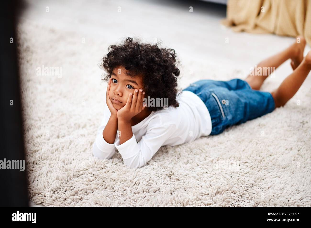 This movie is getting more interesting by the minute. Cropped shot of an adorable little boy lying down on a carpet and watching tv at home. Stock Photo