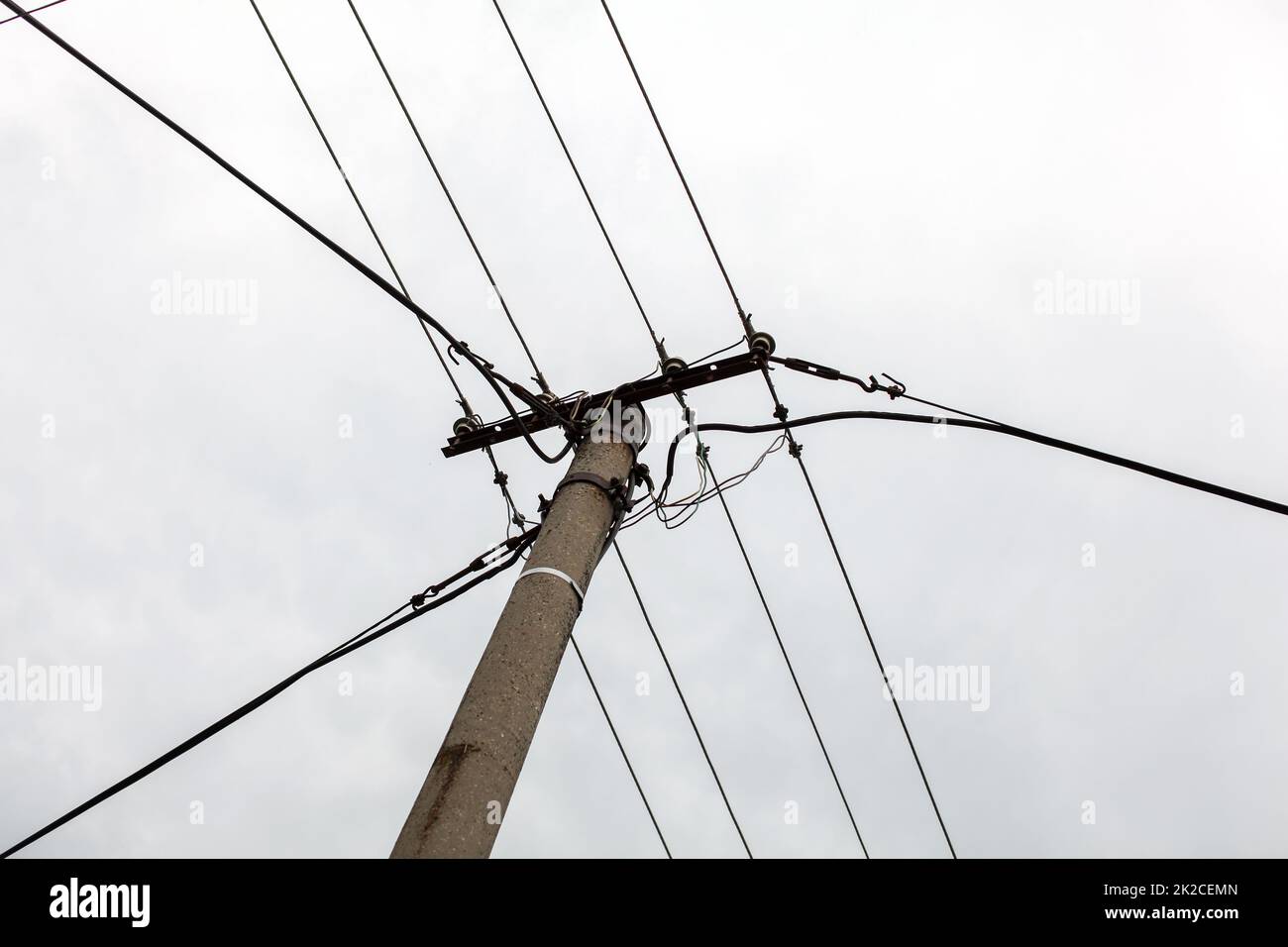 Small concrete pillar with power lines, overcast sky in background. Stock Photo