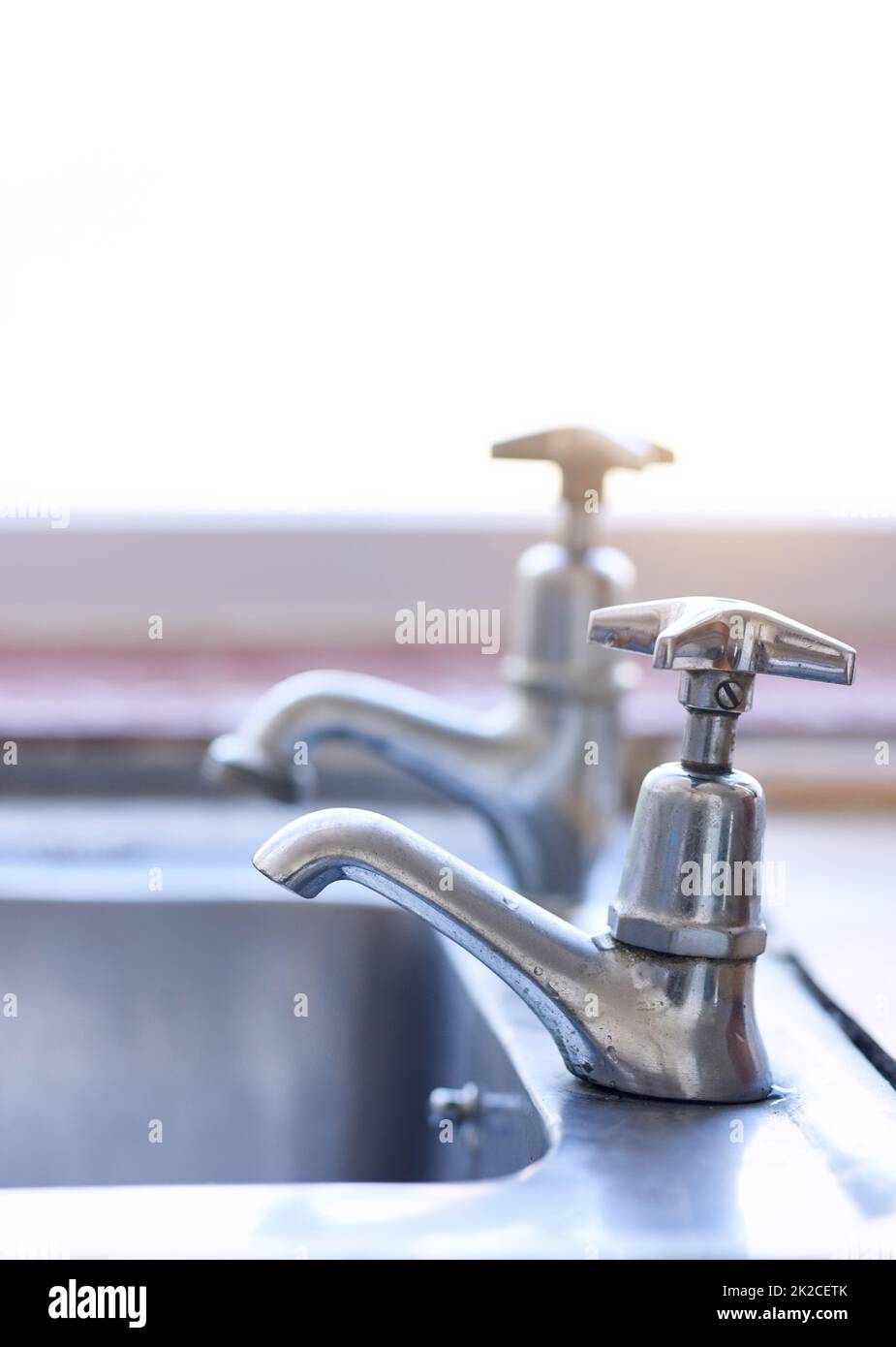 Water is in short supply. Shot of two dripping taps waisting a little bit of water in a basin inside of a house during the day. Stock Photo
