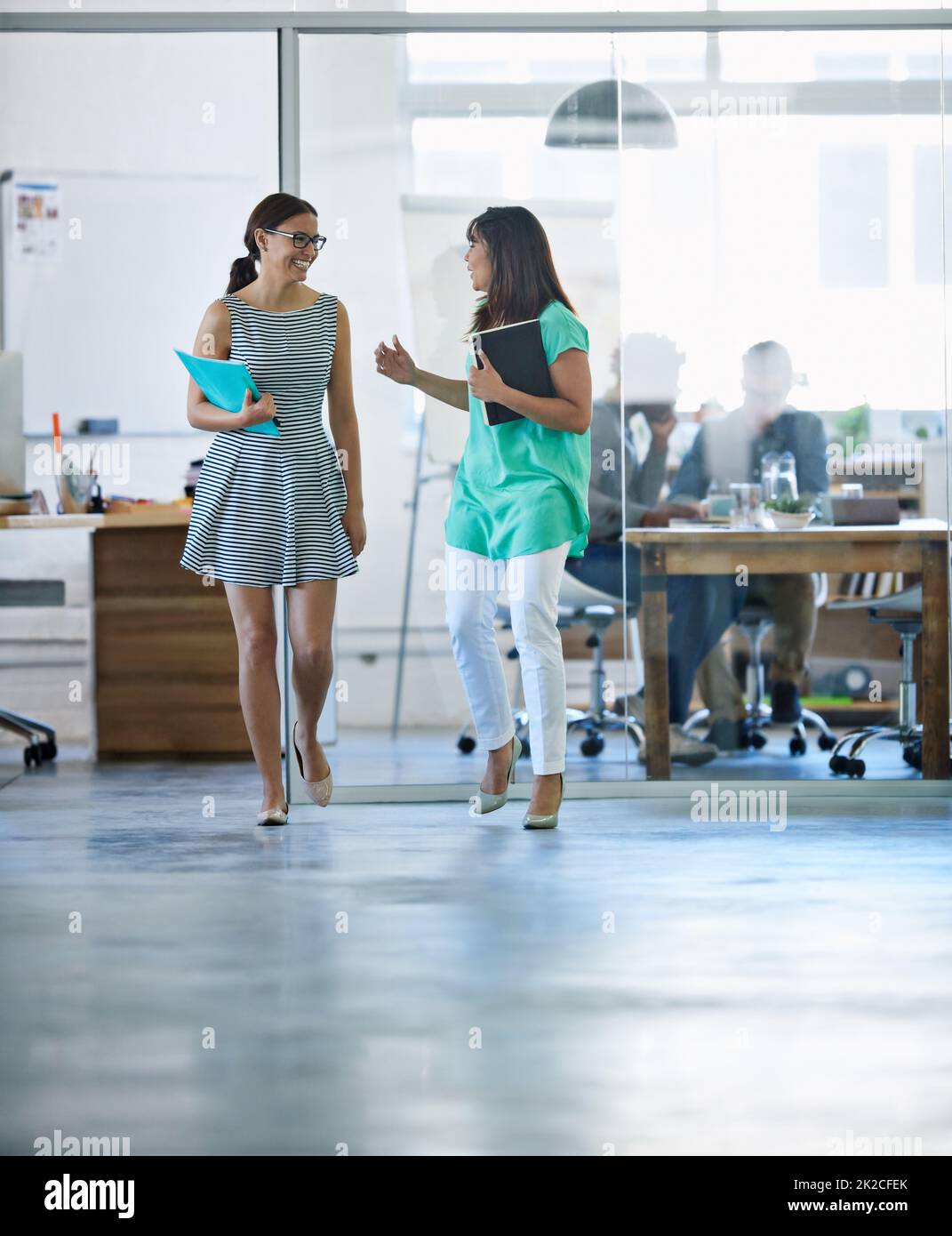 Colleagues and friends. Shot of a two young businesswomen talking while walking through their office. Stock Photo