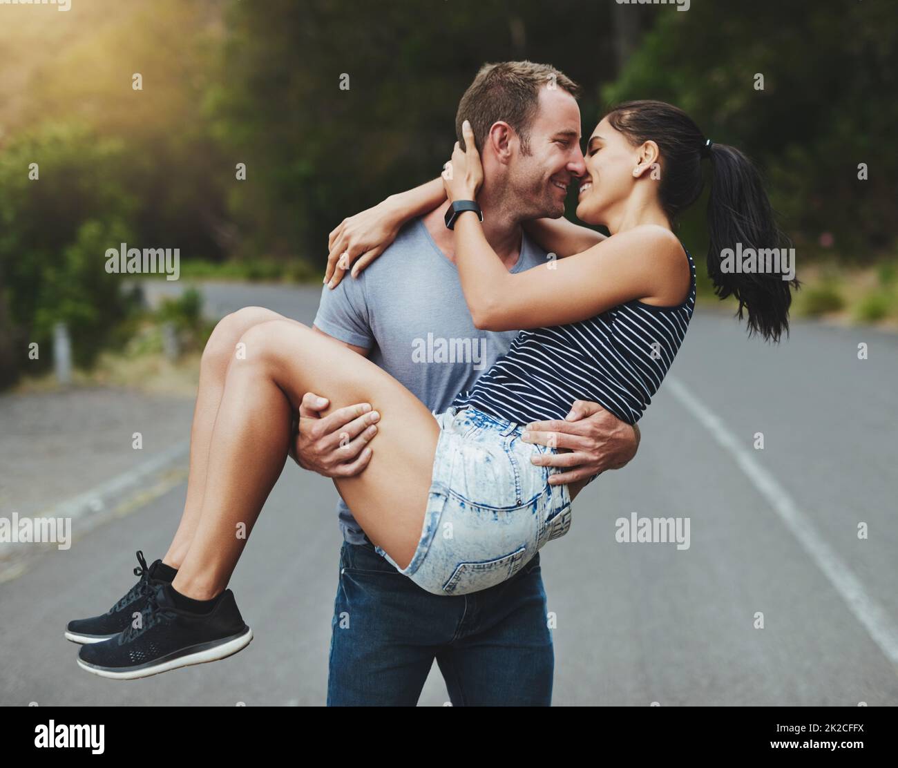 Youre my knight in shining armor. Shot of a young man romantically carrying his girlfriend down a road outdoors. Stock Photo