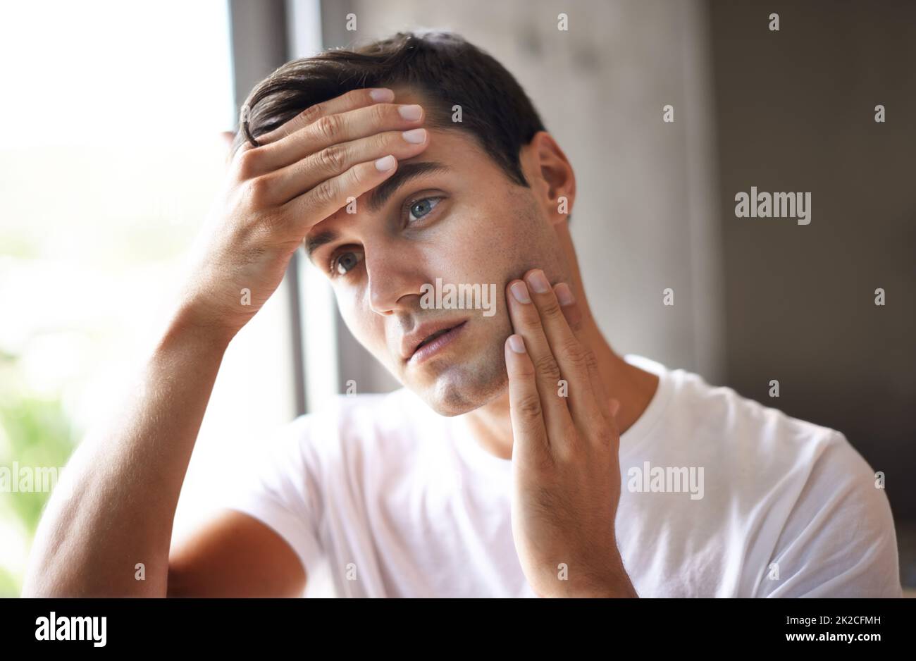 Think I should get this stubble off my face. Cropped shot of a young man feeling his face for stubble. Stock Photo
