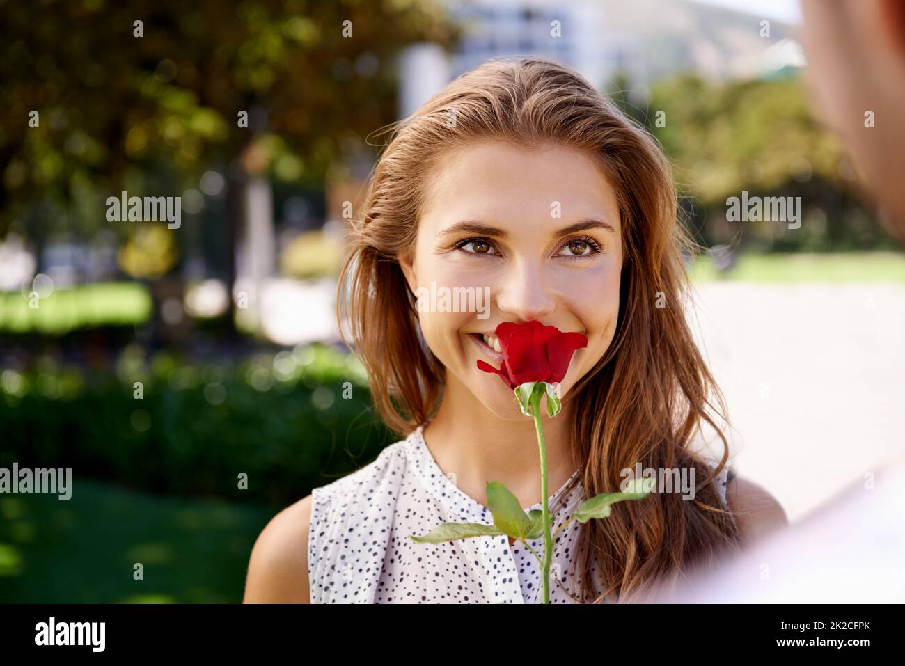 The sweet smell of love. Shot of a young woman smelling a rose her boyfriend is giving here. Stock Photo
