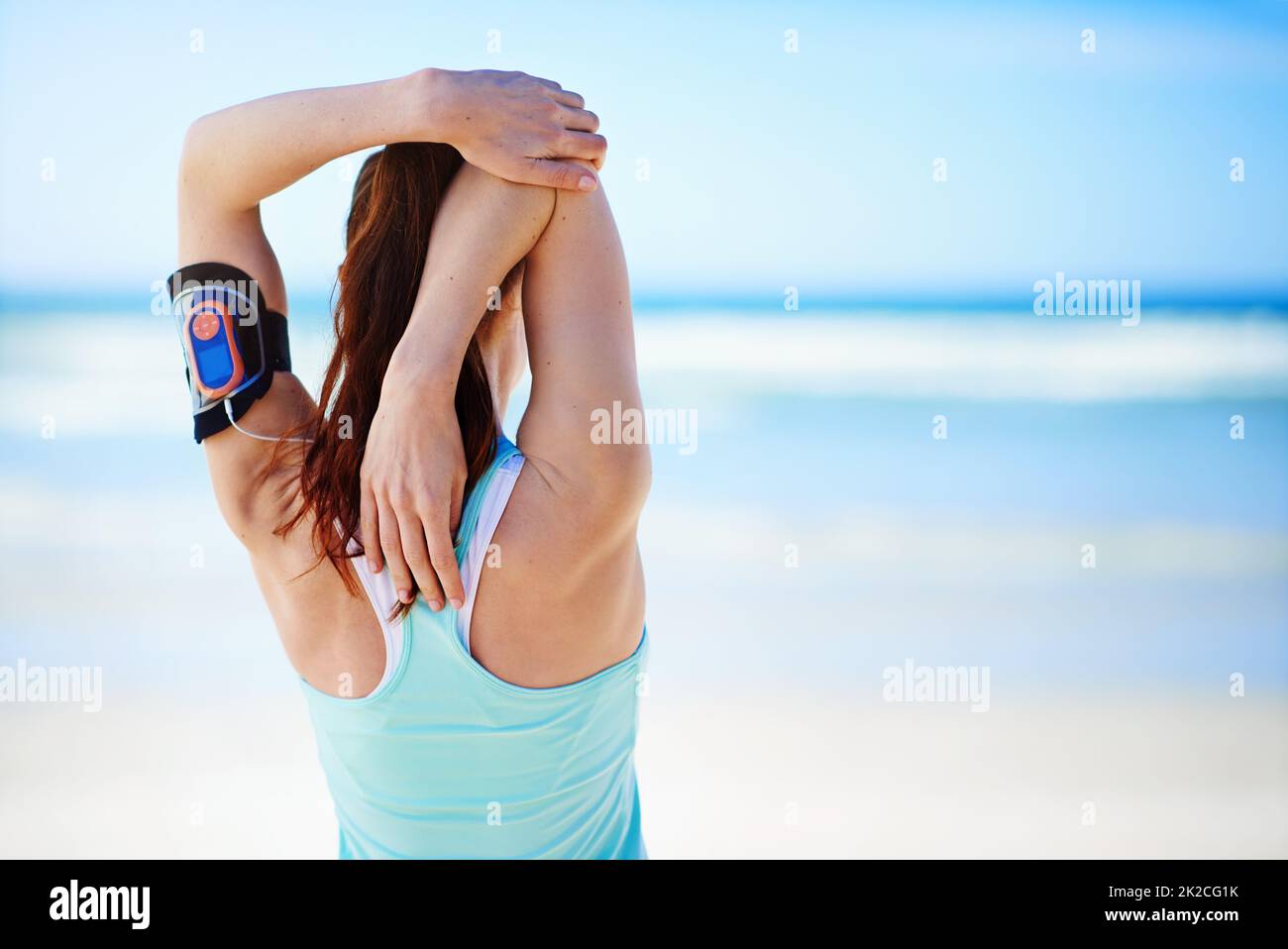 Preparing for a run. Rearview shot of a young woman stretching before a work out on the beach. Stock Photo