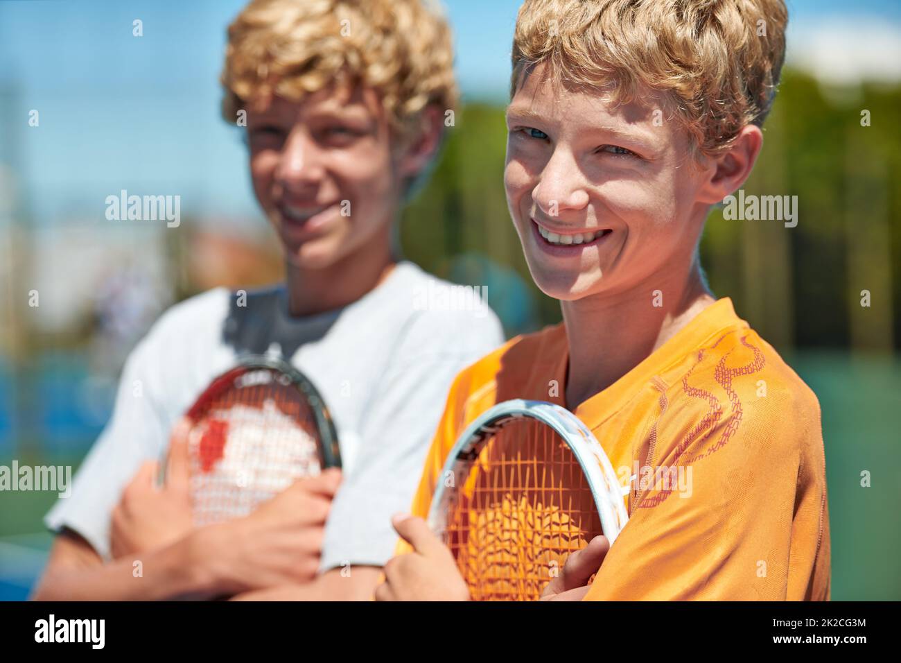Tennis is their sport of choice. Two friends standing together and holding their tennis rackets on the court. Stock Photo
