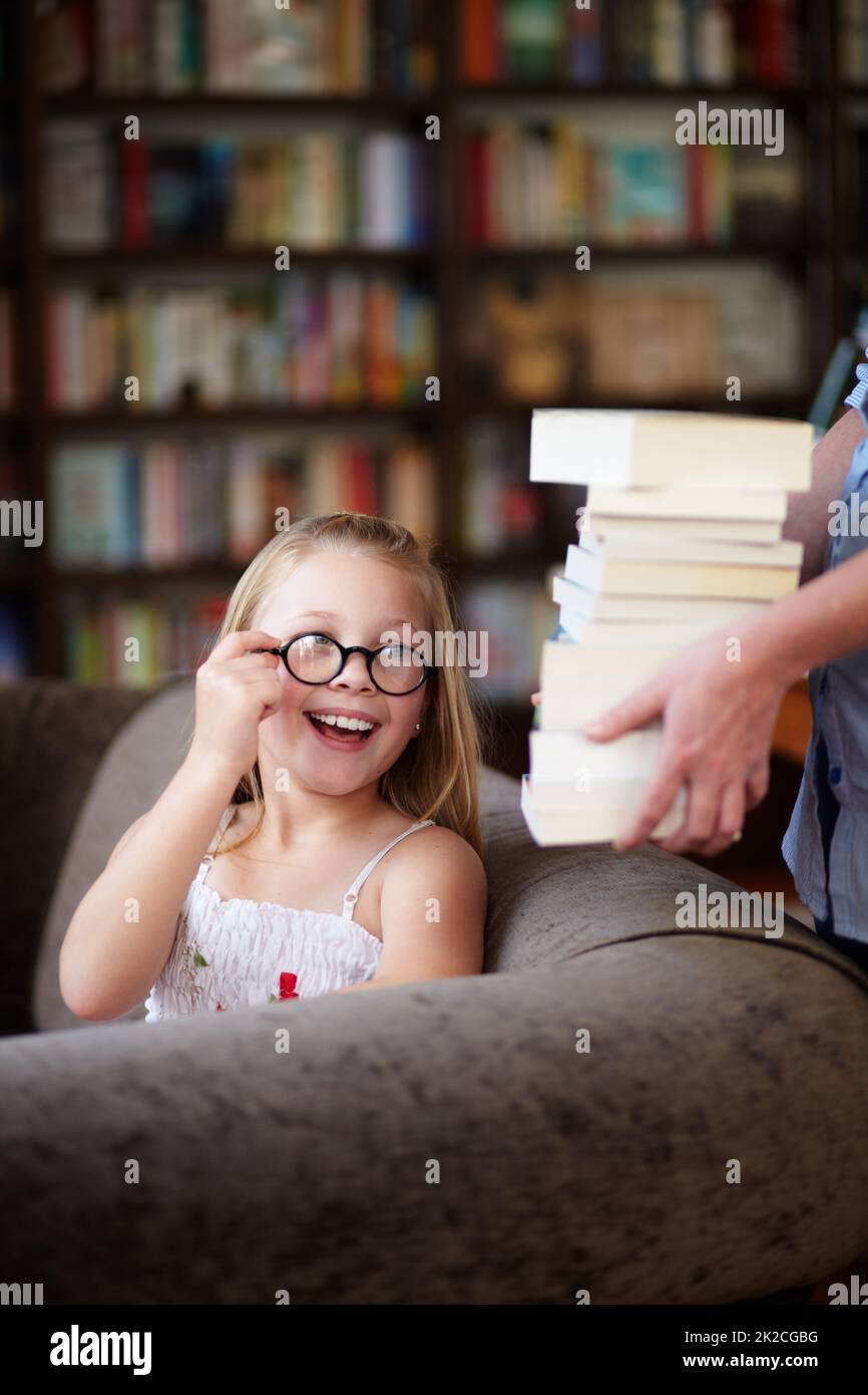 My favourite pastime. A cute little girl wearing glasses smiling as a woman hands her a stack of books. Stock Photo
