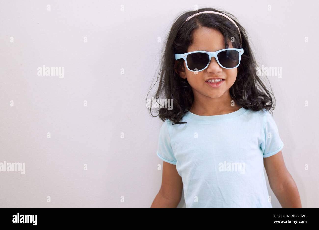 Mom says Im the coolest kid on the block. Shot of an adorable little girl wearing sunglasses while standing against a wall. Stock Photo