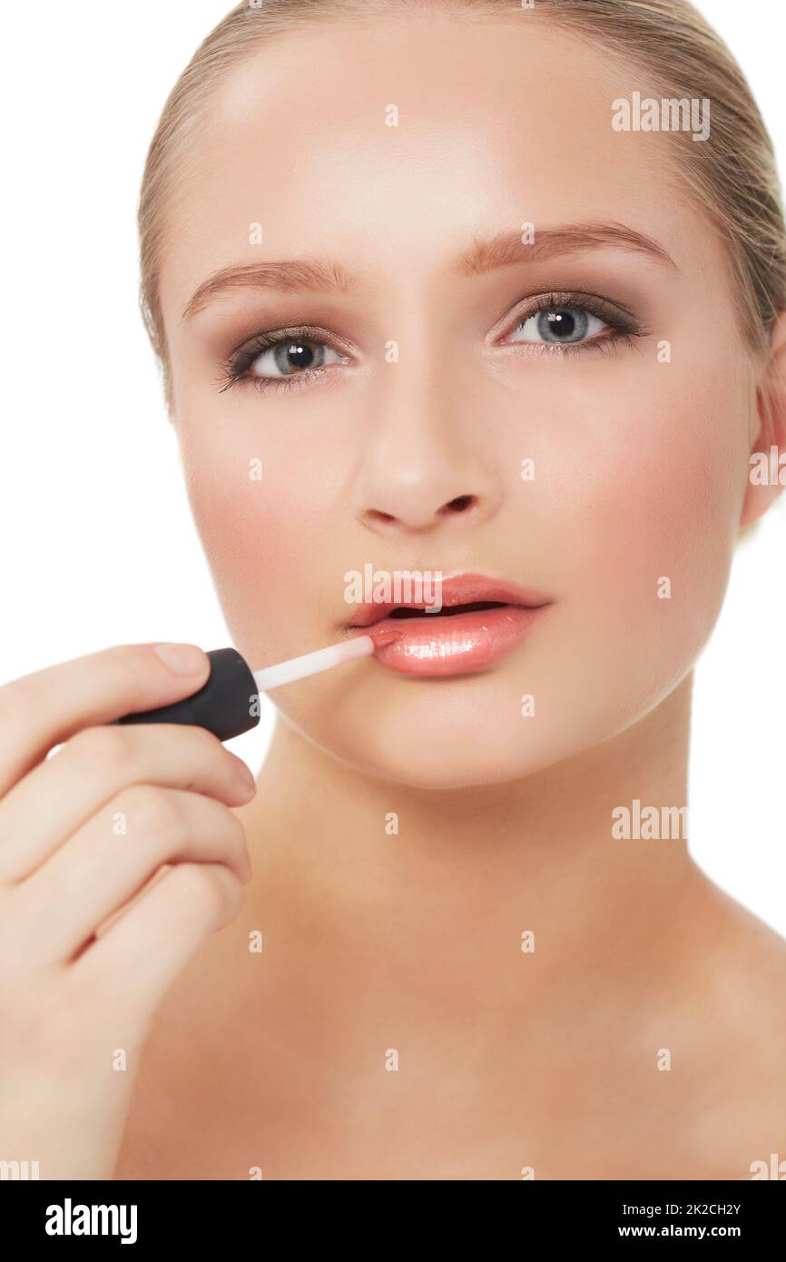 All attention focused on her luscious lips. A stunning young woman applying lipgloss to her luscious lips while isolated on white. Stock Photo