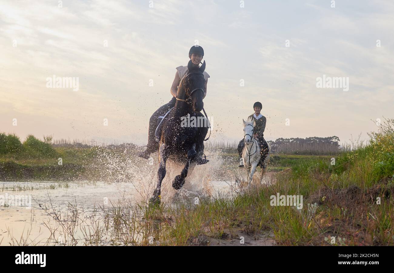 No hour is wasted that is spent in the saddle. Shot of two young women riding their horses outside on a field. Stock Photo