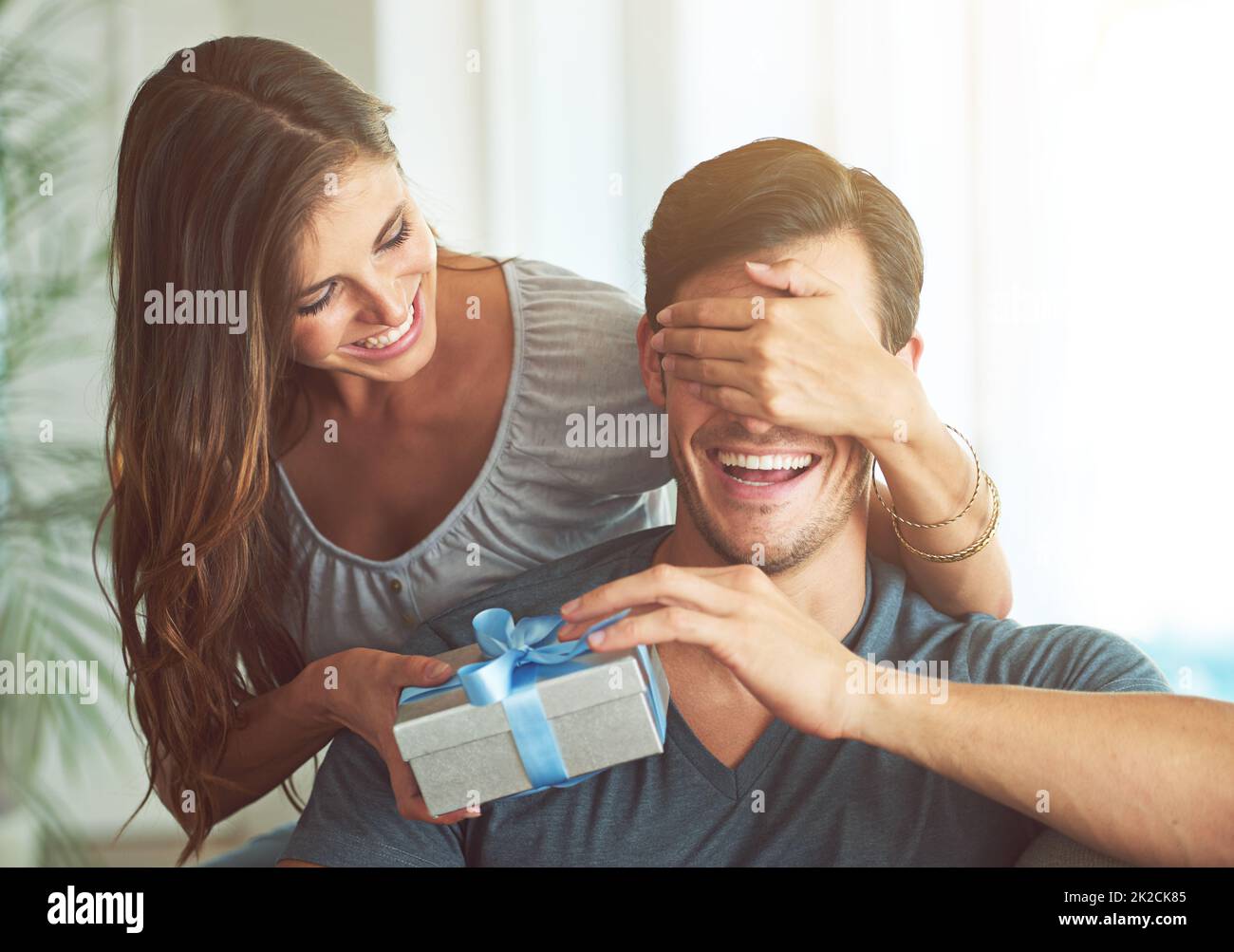 I got you something, honey. A young woman covering her husbands eyes for a surprise gift. Stock Photo