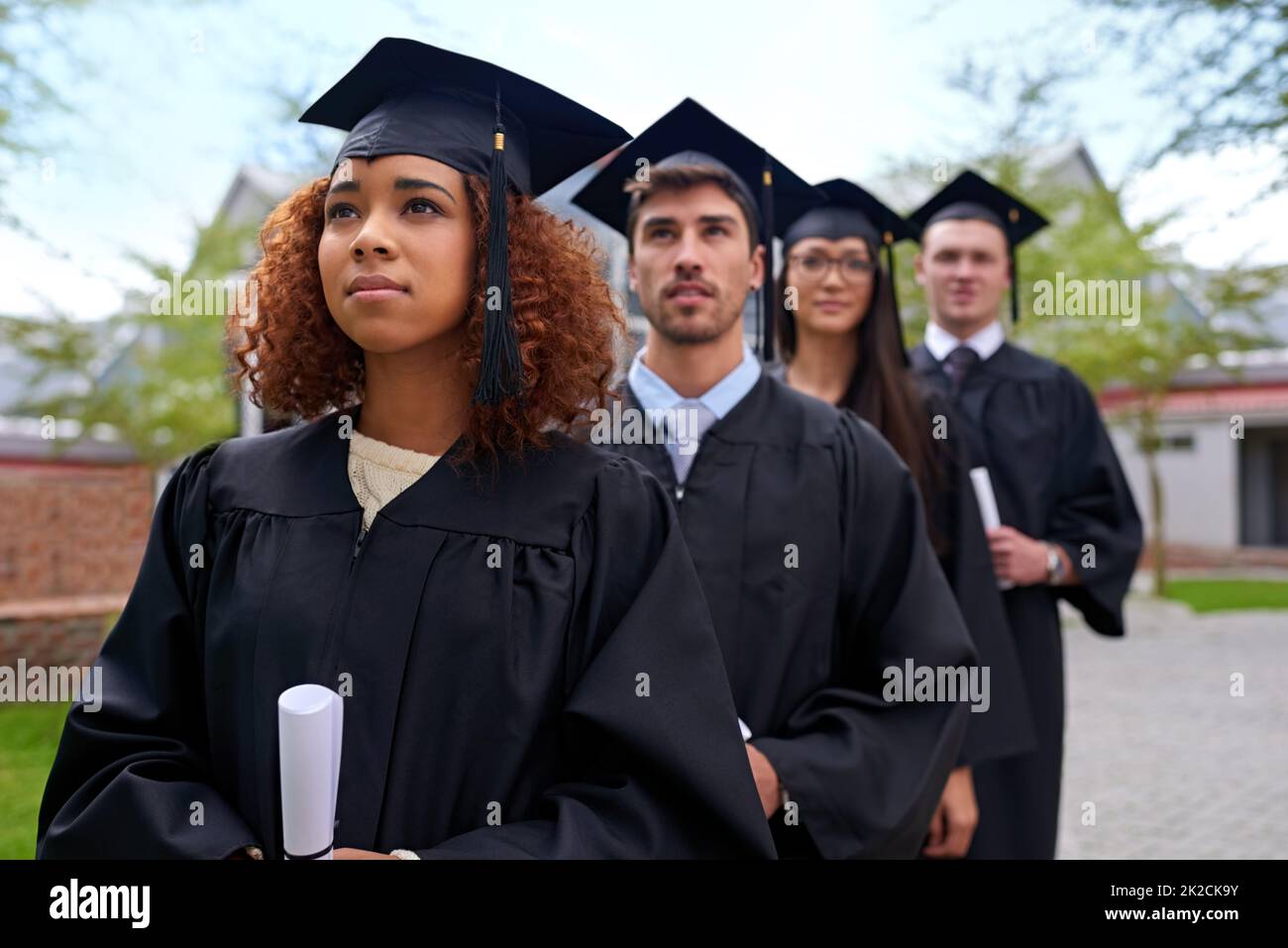 Higher education for high aspirations. Shot of graduating university students standing in a row looking up. Stock Photo
