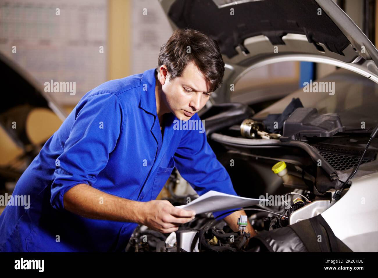 Id better check the wiring. A male mechanic reading some papers while working on the motor of a car. Stock Photo