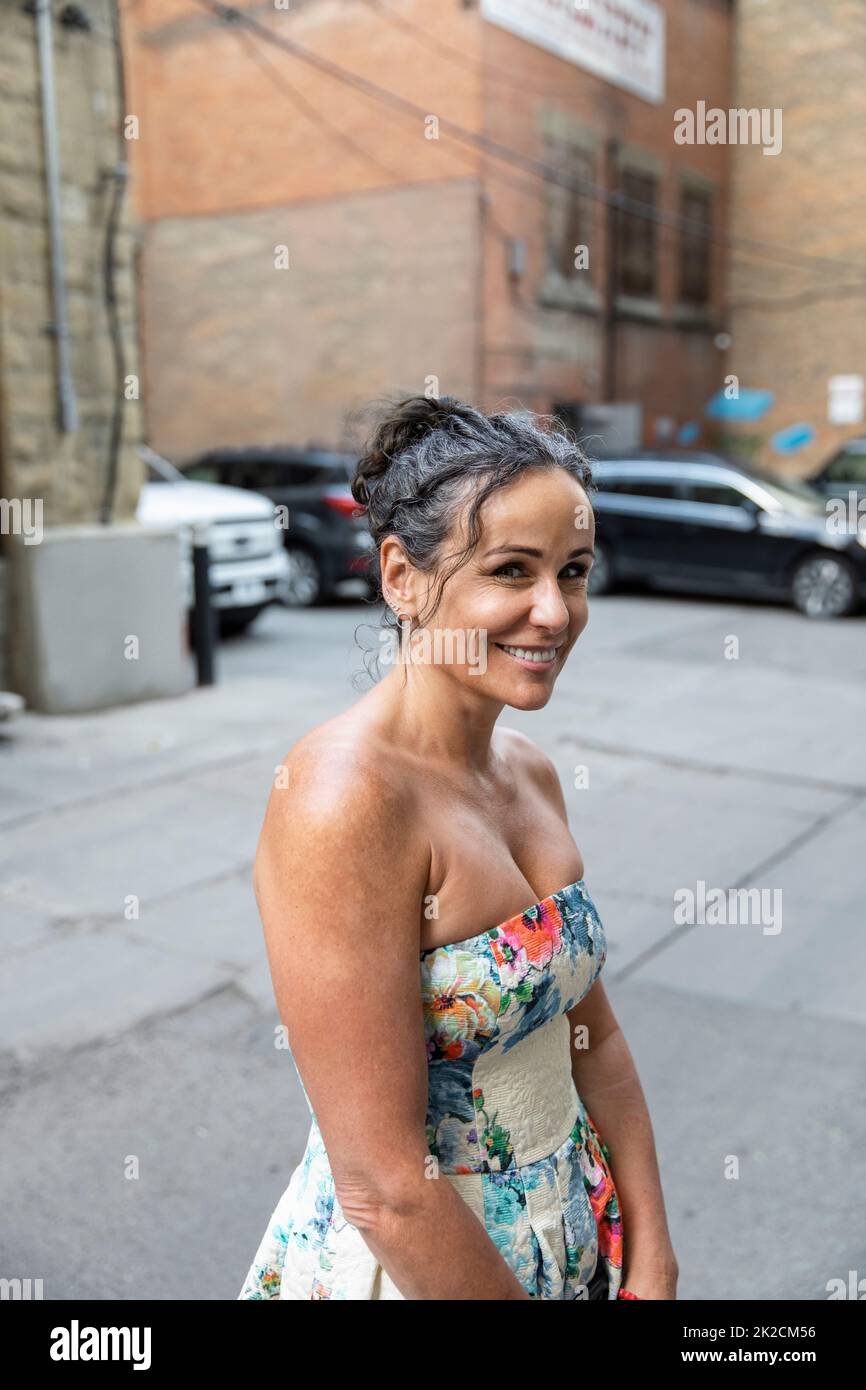 Portrait smiling woman in floral dress in urban alley Stock Photo