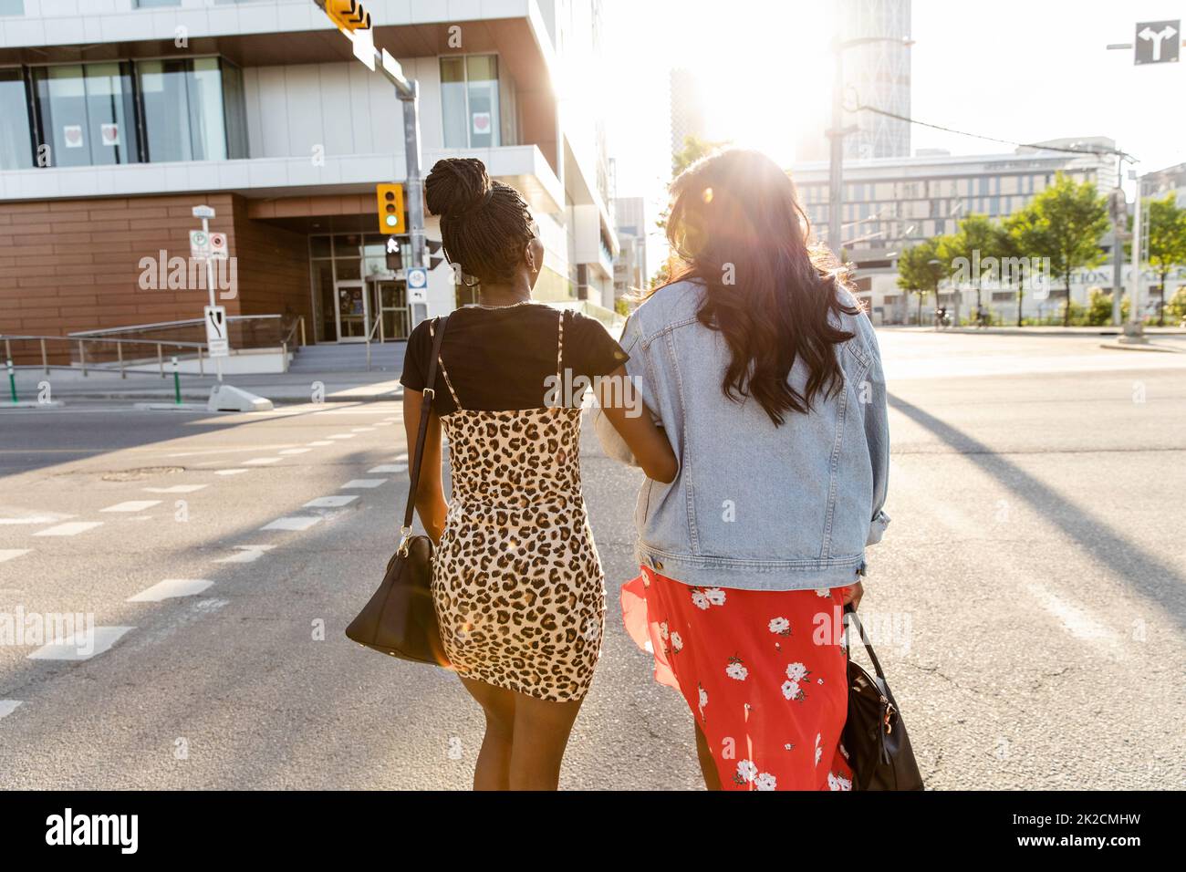 Young women friends crossing sunny city street arm in arm Stock Photo