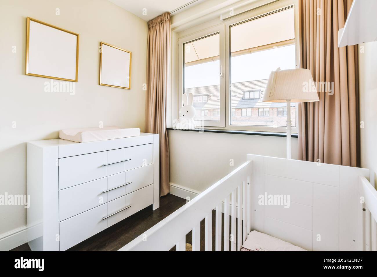 Interior of white room with baby crib near window with blue chest of