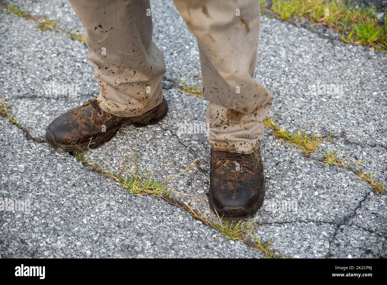 A man in splattered work boots and pants on broken asphalt street Stock Photo