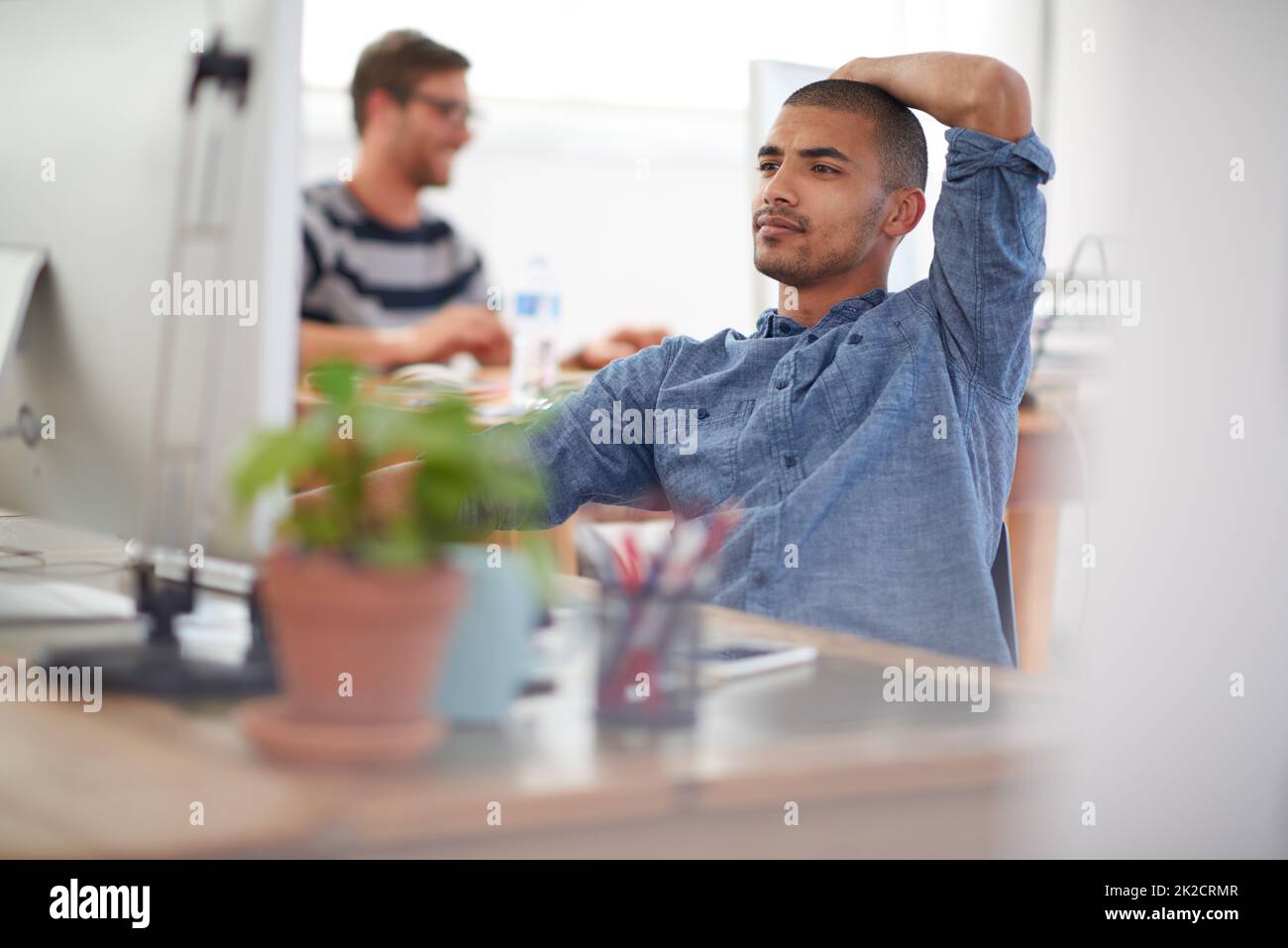 Trouble shooting modern problems. Serious young multi-ethnic man working at his desk in an open plan work space. Stock Photo