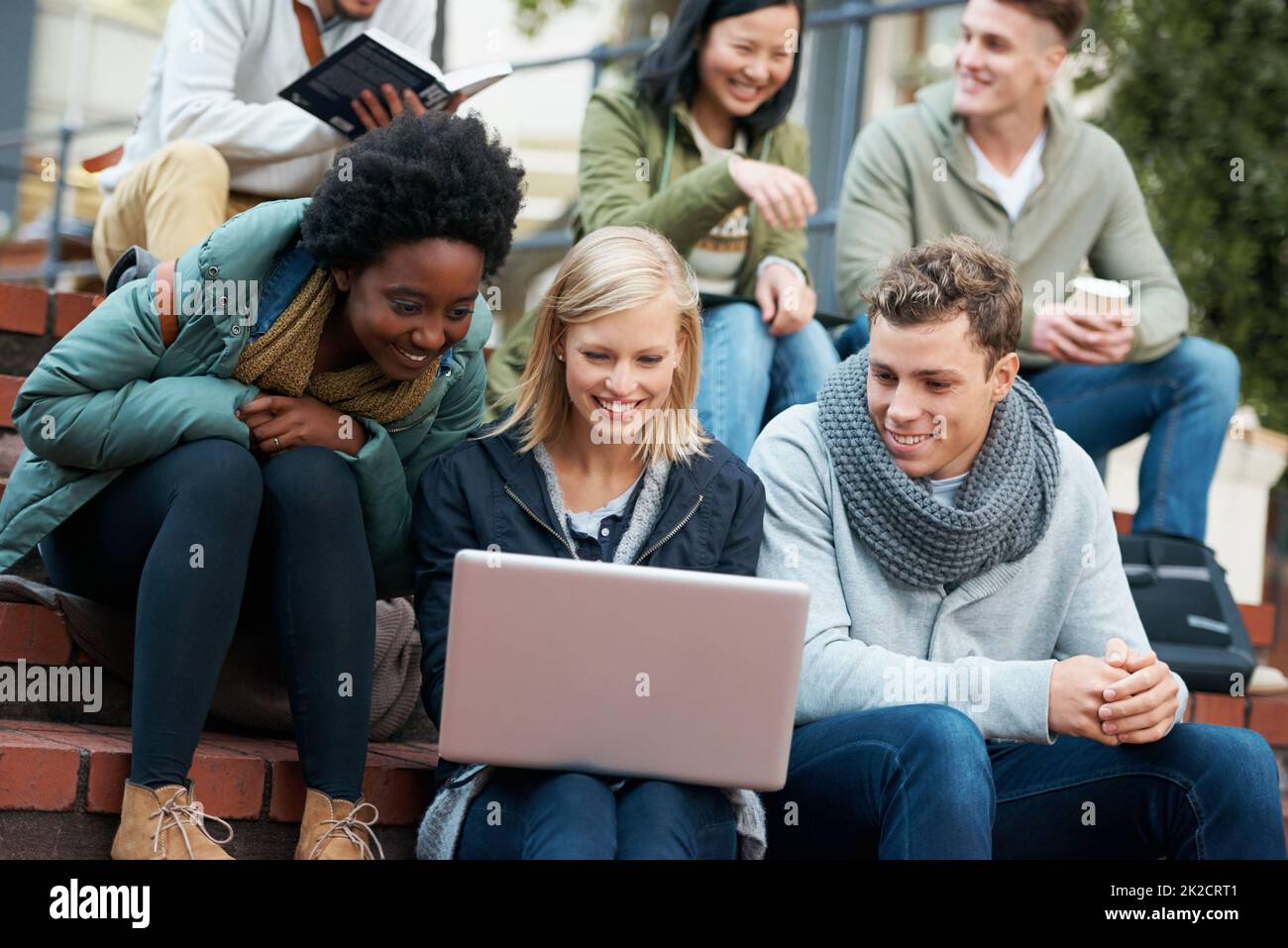 We are eager to learn. Shot of a group of smiling university students looking at something on a laptop. Stock Photo