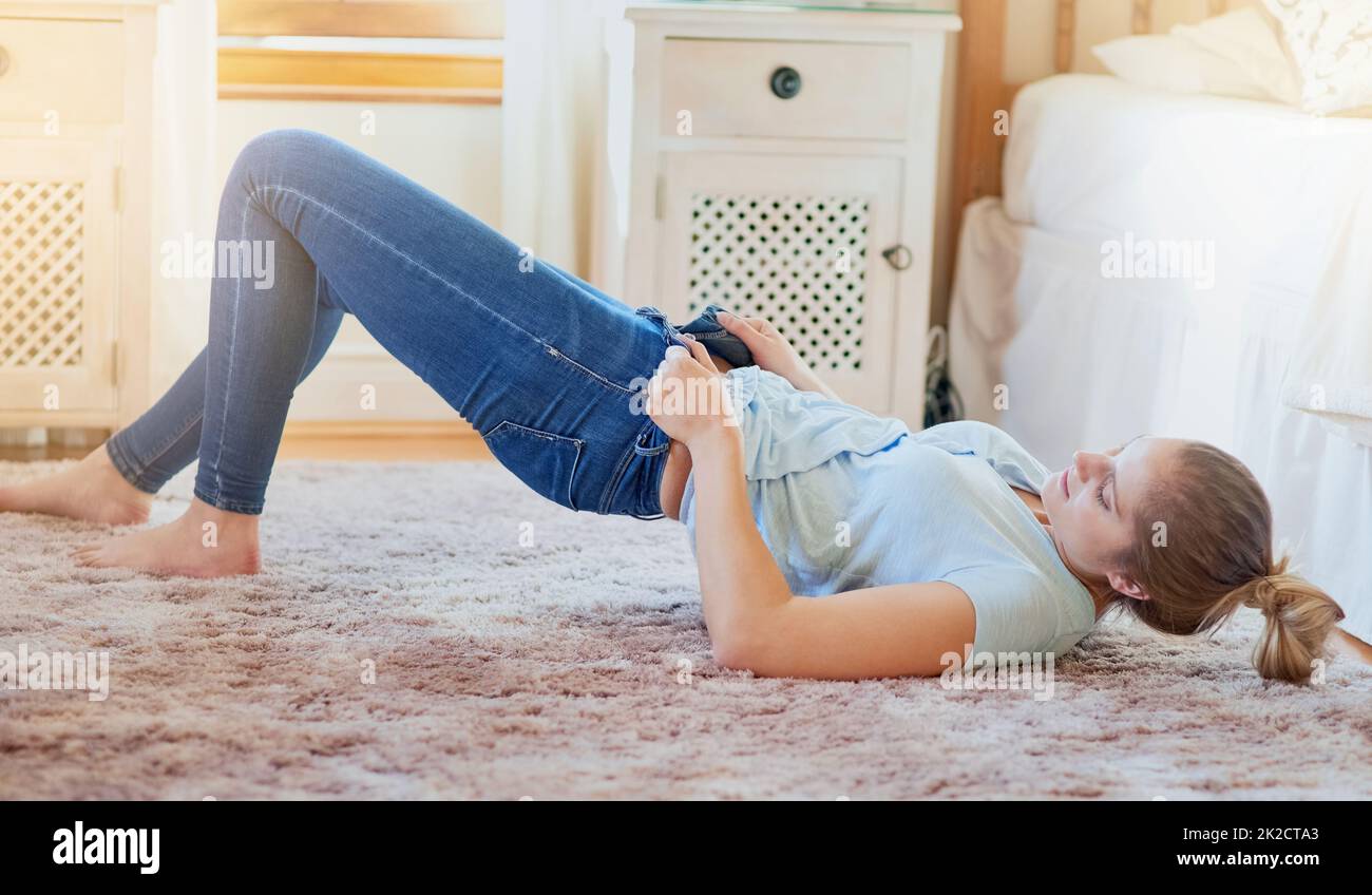 The struggle is real. Shot of a young woman struggling to fit into her jeans at home. Stock Photo