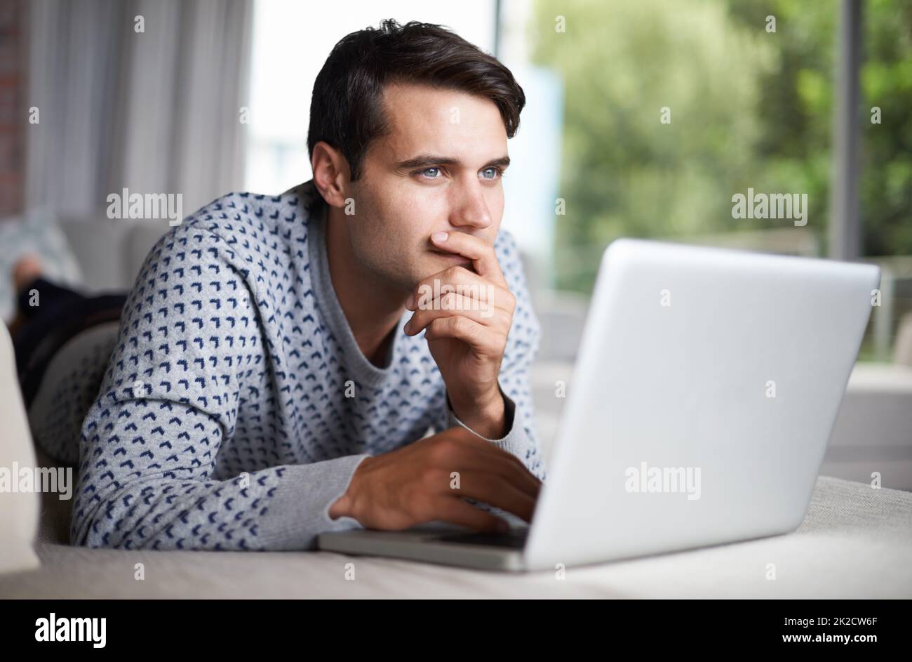 When you try to remember what your password is.... Shot of a young man contemplating while using his laptop. Stock Photo