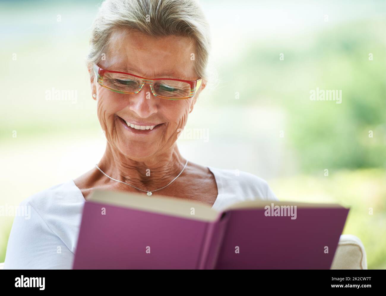 This is such a great story. A delighted woman reading an enjoyable book in her lounge. Stock Photo