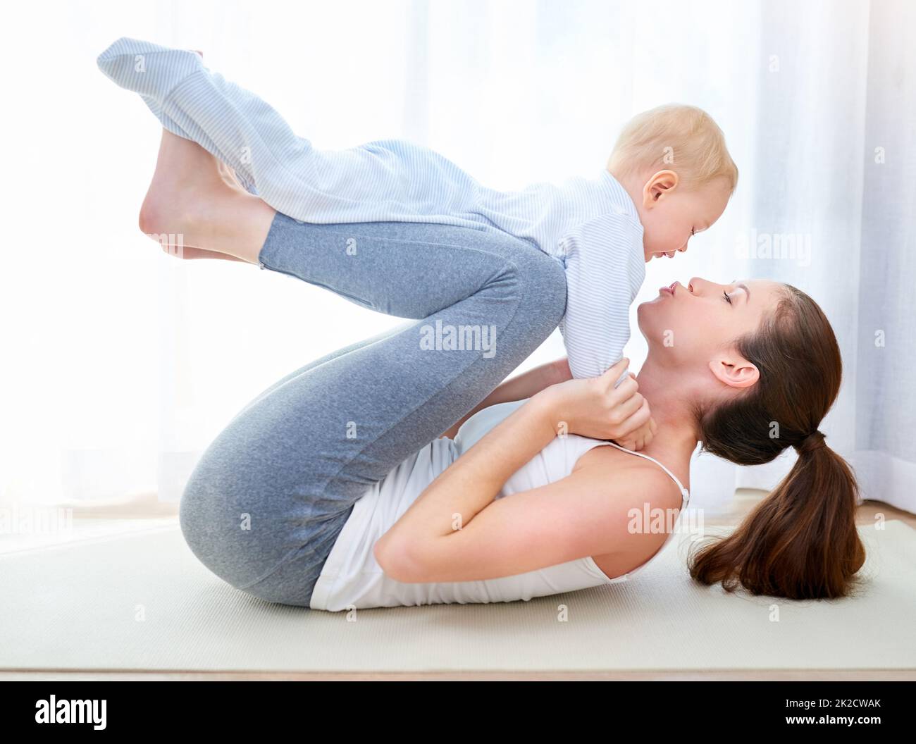 Youre gonna have to work harder for that kiss mom. Shot of a young woman working out while spending time with her baby boy. Stock Photo