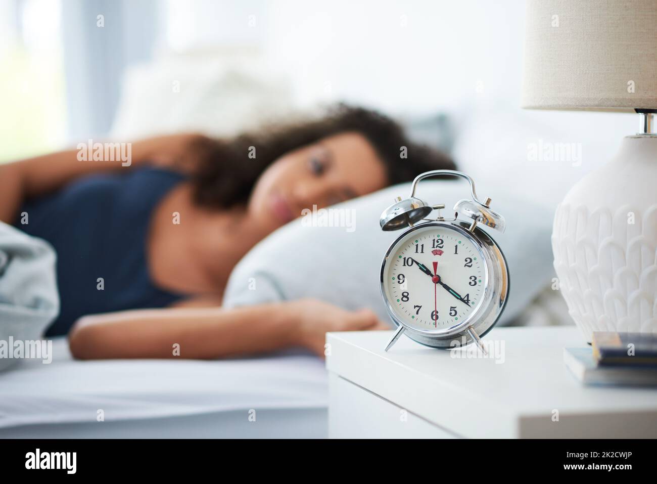 The alarm clock, the thief of the best sleep. Shot of an attractive young woman laying in bed with an alarm clock on her bedside table. Stock Photo