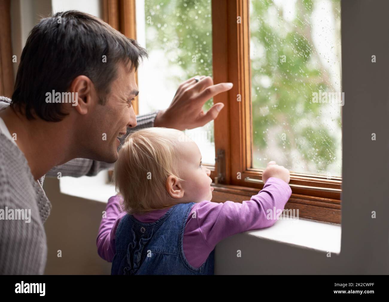 Look at what a beautiful day it is outside. A young father and his baby girl looking at something beyond the window. Stock Photo