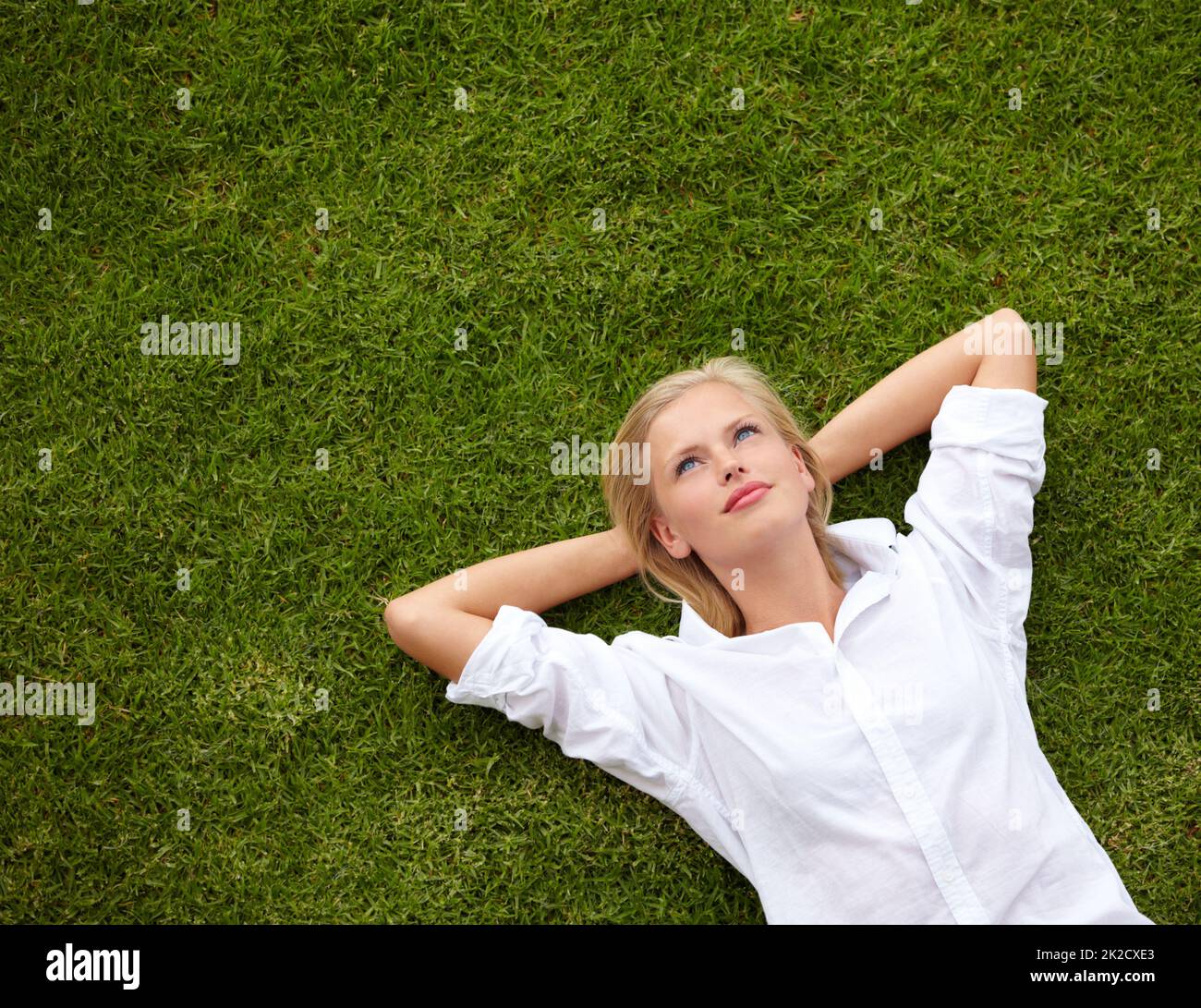 So much to ponder.... High angle shot of an attractive young woman relaxing on a grassy field and looking up at the sky. Stock Photo