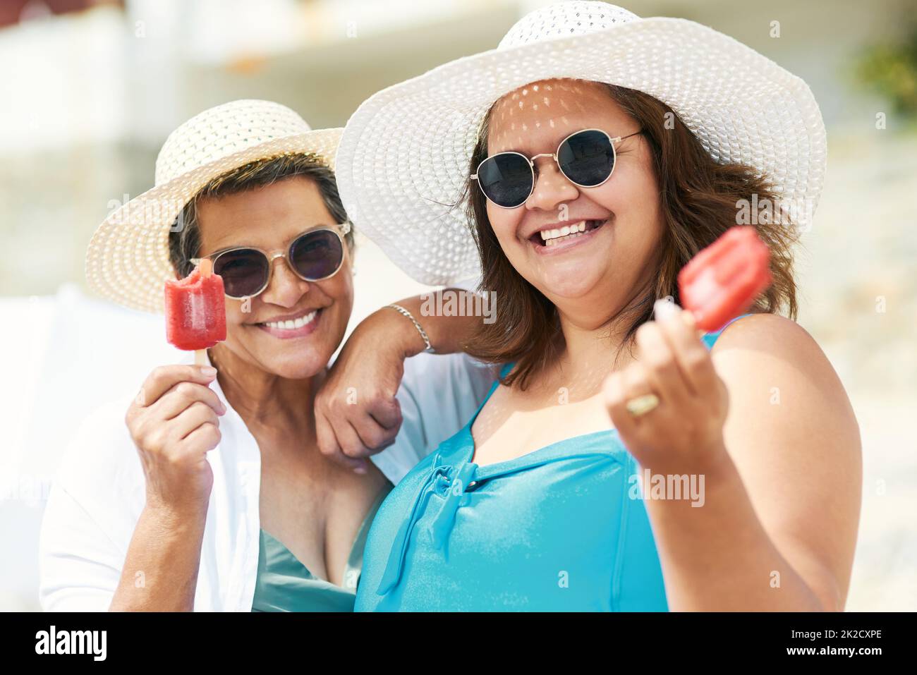 The perfect summer cool down. Shot of two mature friends standing together and enjoying ice cream while bonding on the beach during the day. Stock Photo