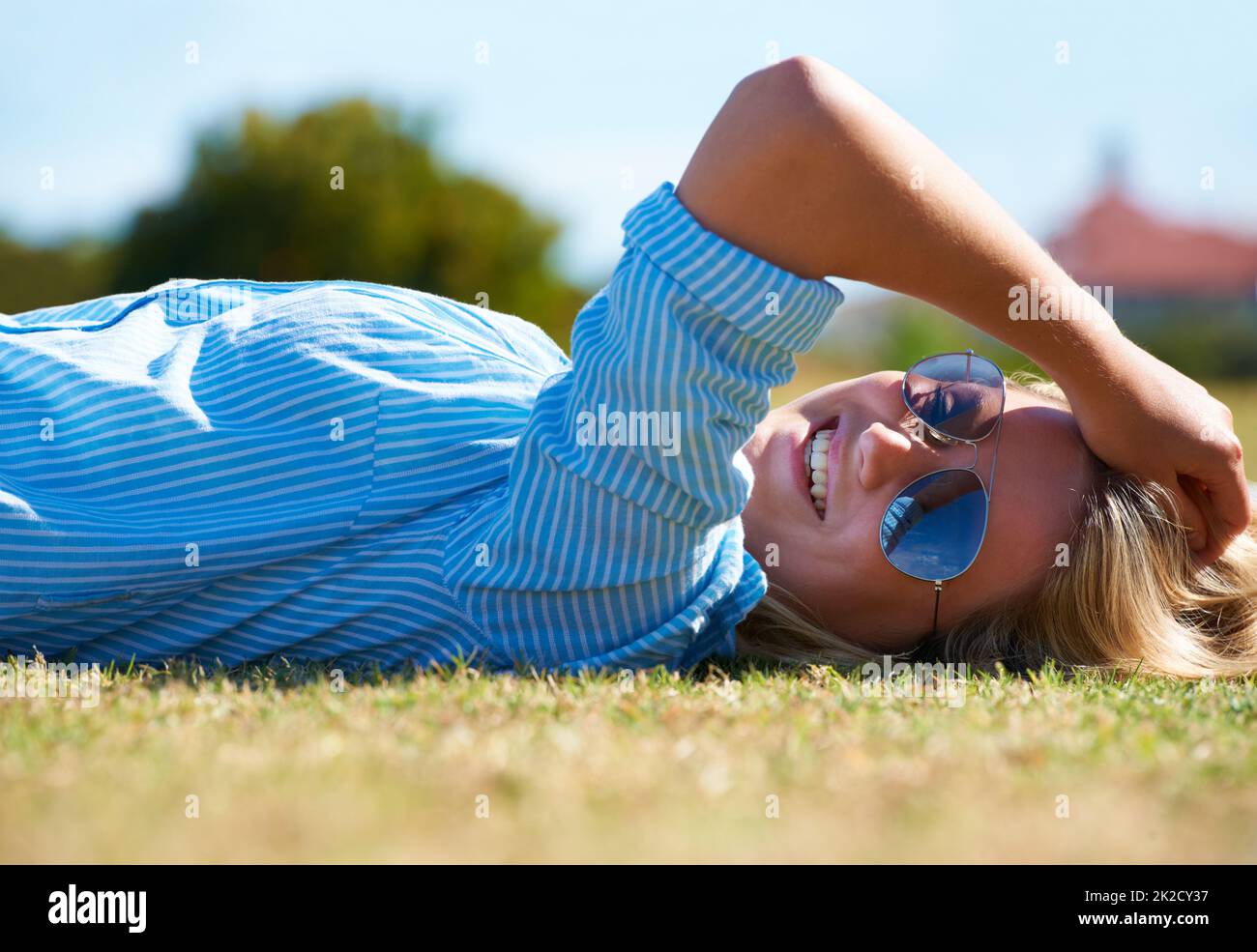 Summers finally here. A happy woman lying on a patch of grass in the sunshine. Stock Photo