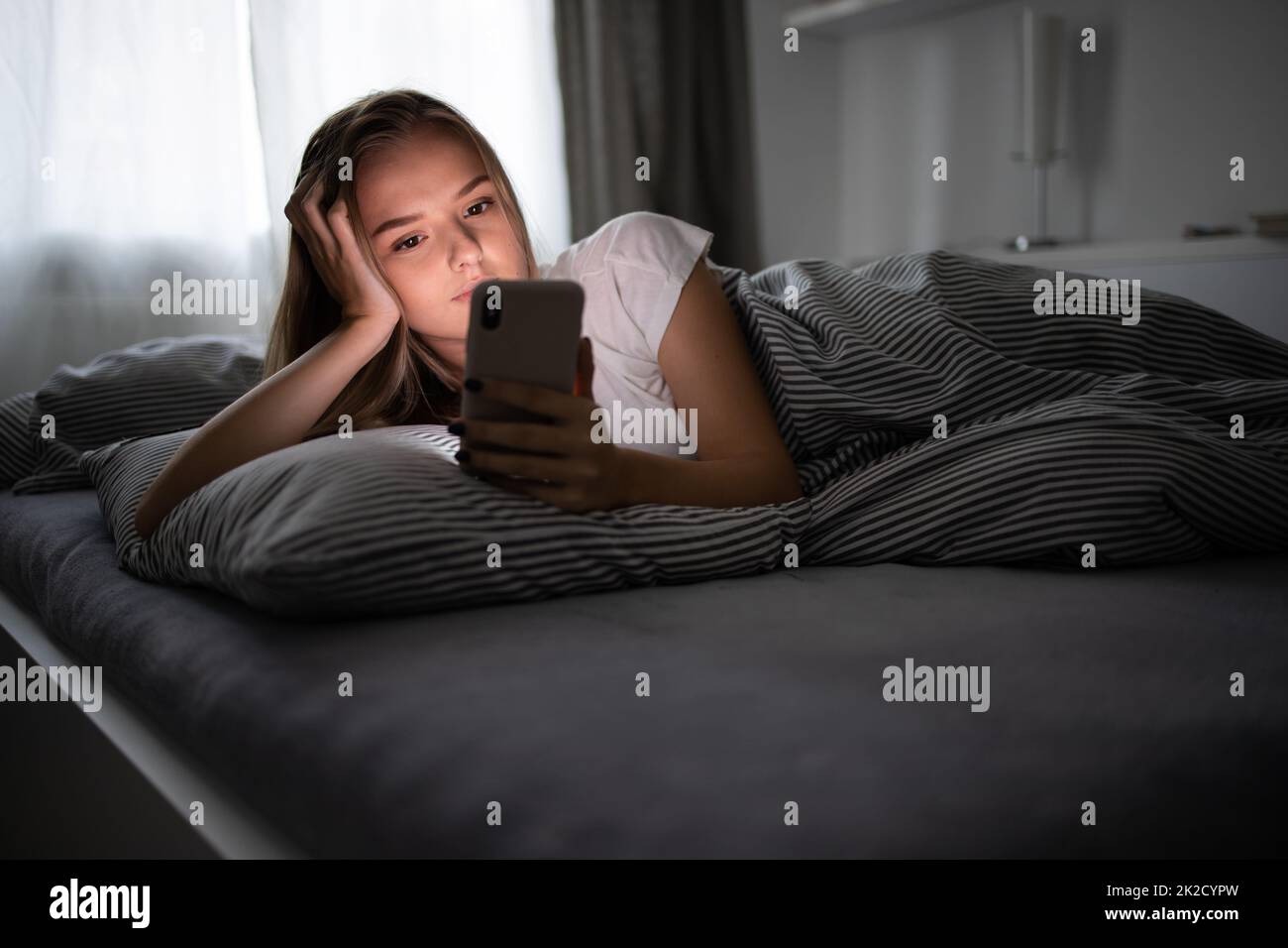 Pretty, young woman  in her bed with her cell phone. Smartphone in Bed Mobile/smartphone  Addiction Concept. Stock Photo