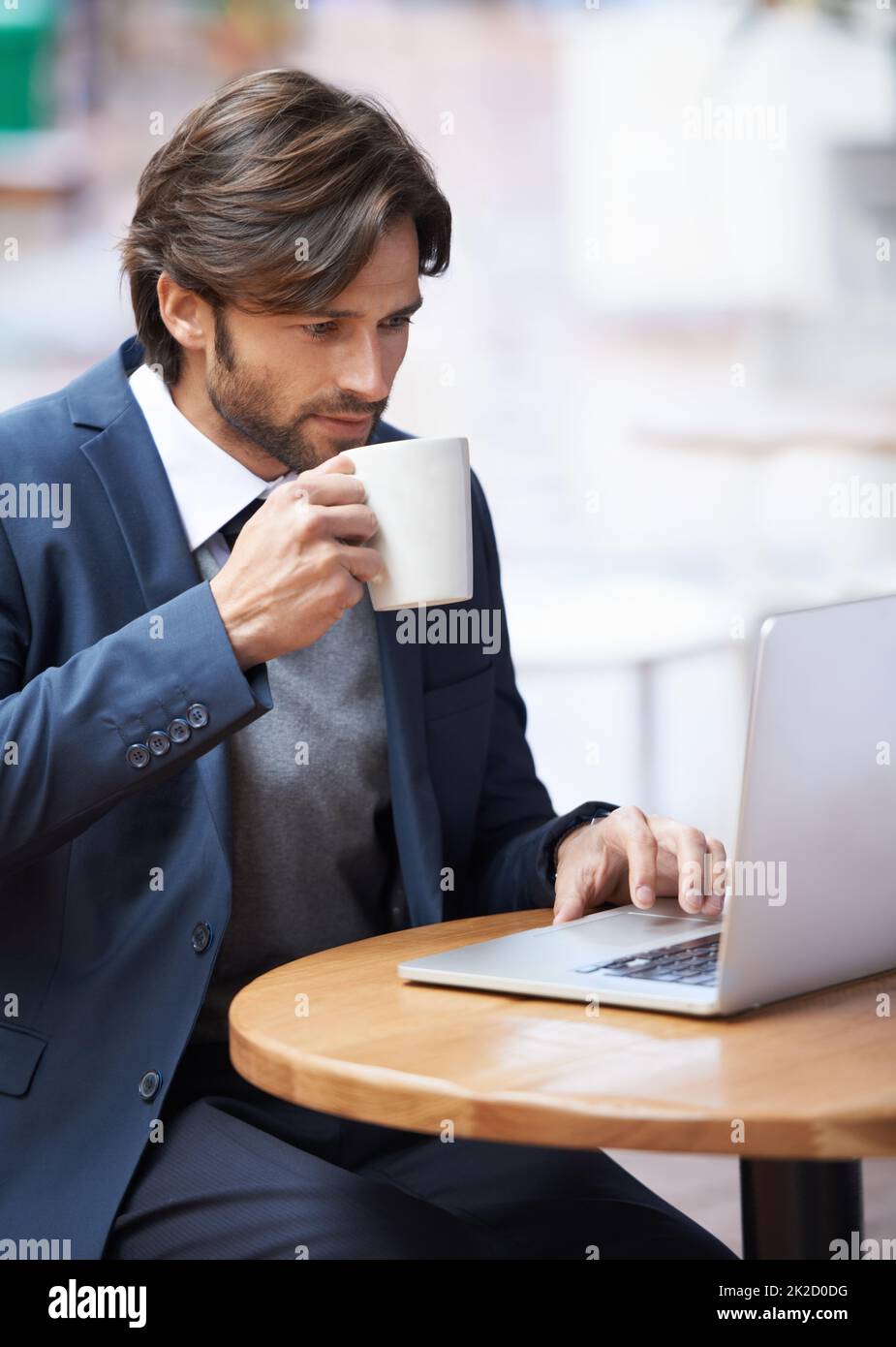 Some casual browsing during my lunch hour. A handsome businessman working on his laptop and drinking coffee at a coffeeshop. Stock Photo