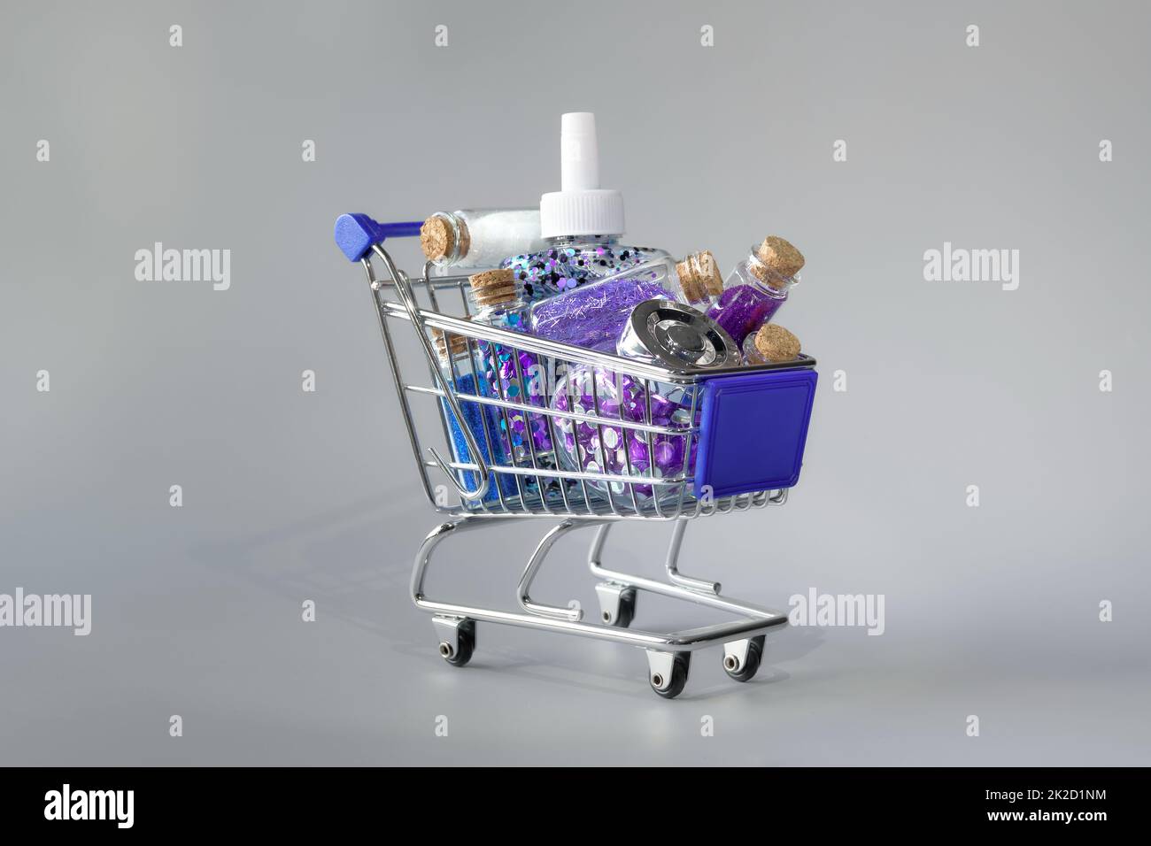 Cost of glitter products. Mini shopping cart with several glitter bottles on abstract neon blue pink background. Stock Photo