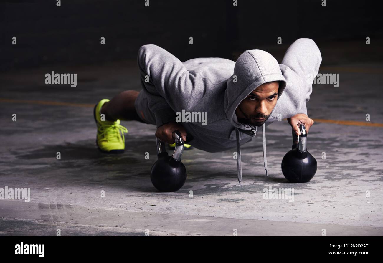 Focussed on his workout. Shot of a young man doing push-ups with kettle bell weights. Stock Photo