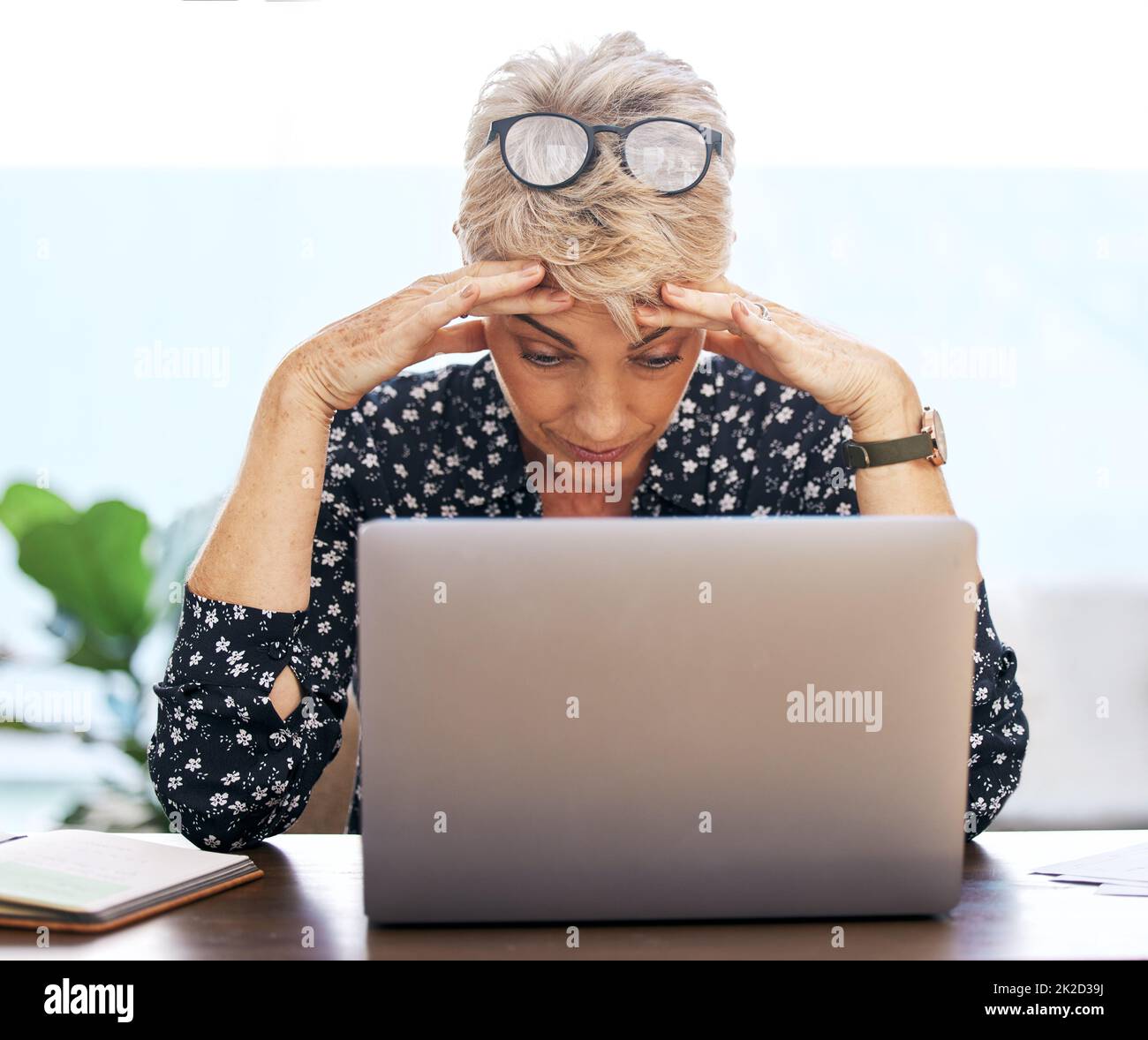 This cannot be happening right now. Shot of a mature woman sitting alone and feeling stressed while using her laptop to work from home. Stock Photo