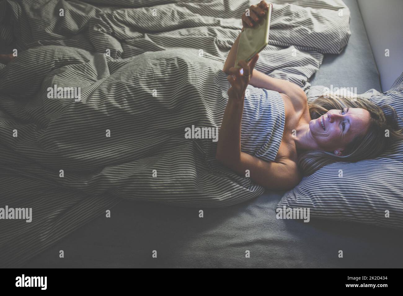 Middle-aged woman using her tablet computer before sleep in bed in the evening - exposure to blue light right before sleep Stock Photo