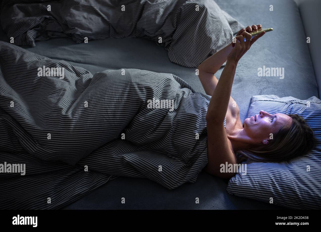 Middle-aged woman using her tablet computer before sleep in bed in the evening - exposure to blue light right before sleep Stock Photo
