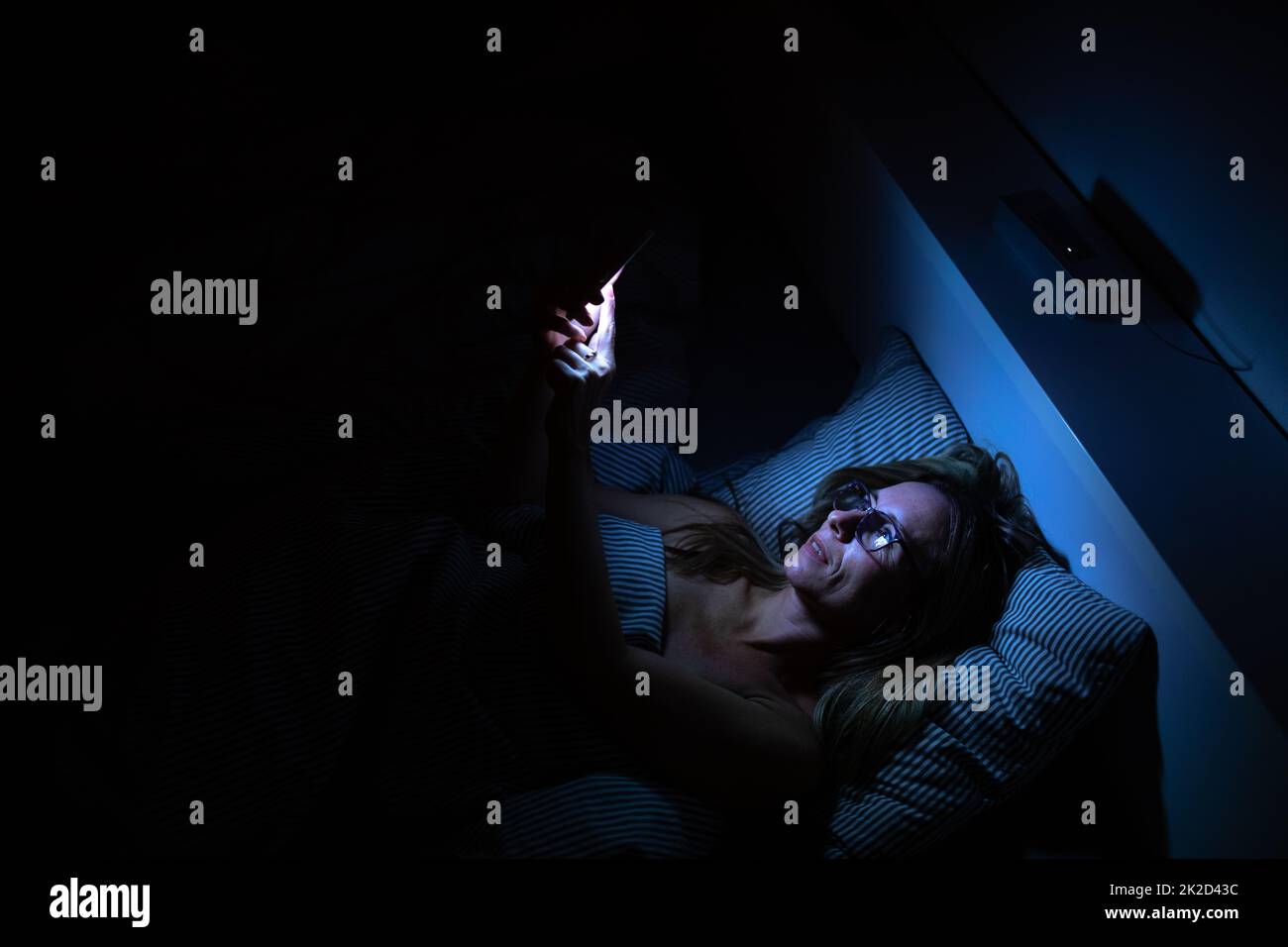 Pretty, middle-aged woman using her cell phone in bed at night - unhealthy blue light exposure Stock Photo
