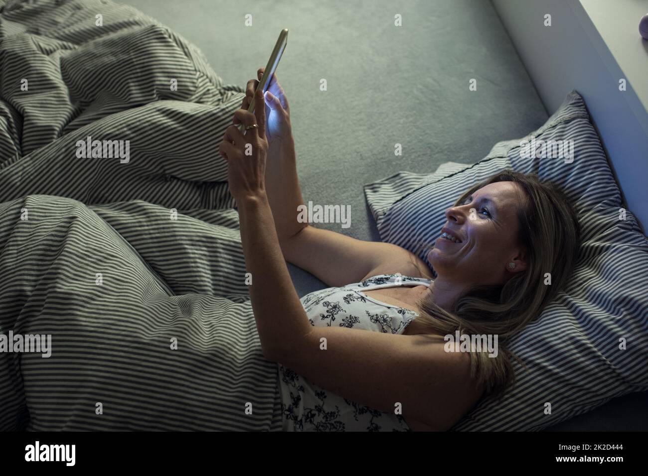 Pretty, middle-aged woman using her tablet computer before sleep in bed in the evening Stock Photo