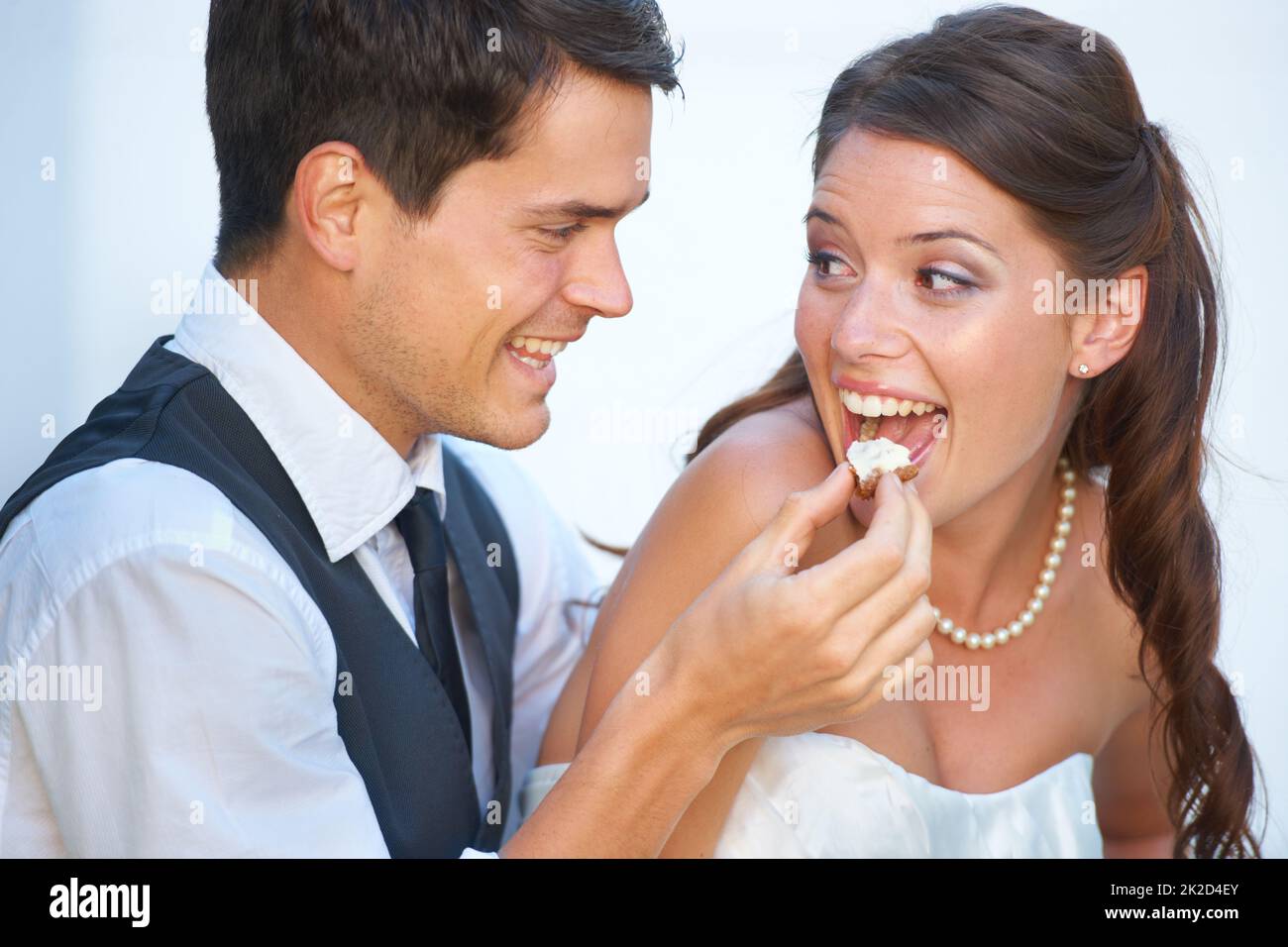 Playful reception moment. Fun shot of a young groom feeding his bride wedding cake. Stock Photo