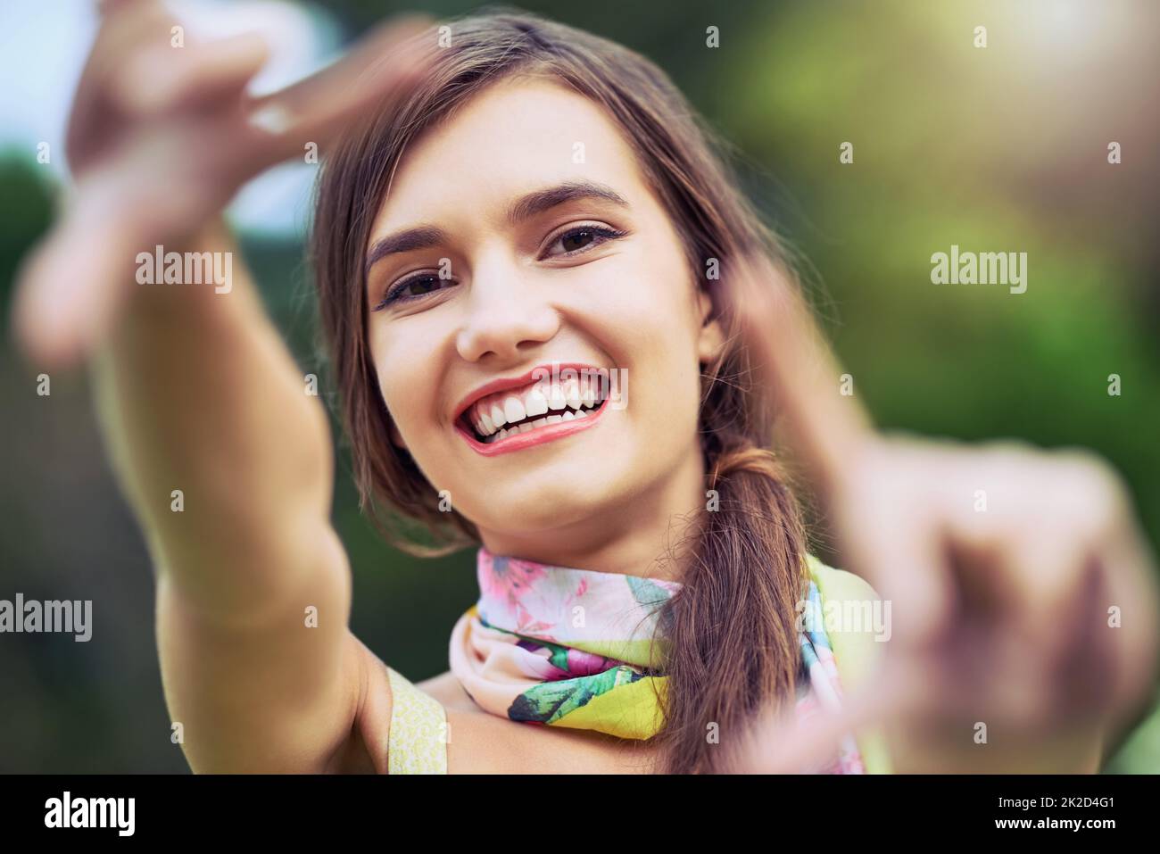 Picture perfect. Portrait of a cheerful young woman making a frame shape with her hands while looking at the camera outside during the day. Stock Photo